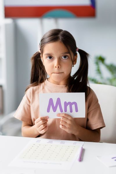 Girl with pigtails holding a card with the letter