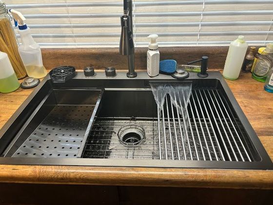 A stainless steel kitchen sink is sitting on a wooden counter next to a window.