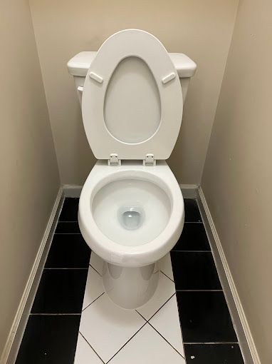 A white toilet is sitting on a black and white tiled floor in a bathroom.