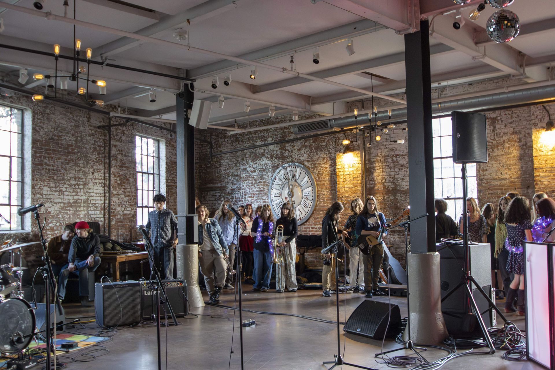 Band performing for a crowd in a brick-walled venue with industrial elements; people watching and listening.
