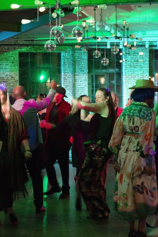 People dancing at a party; green lights, disco balls, brick walls.
