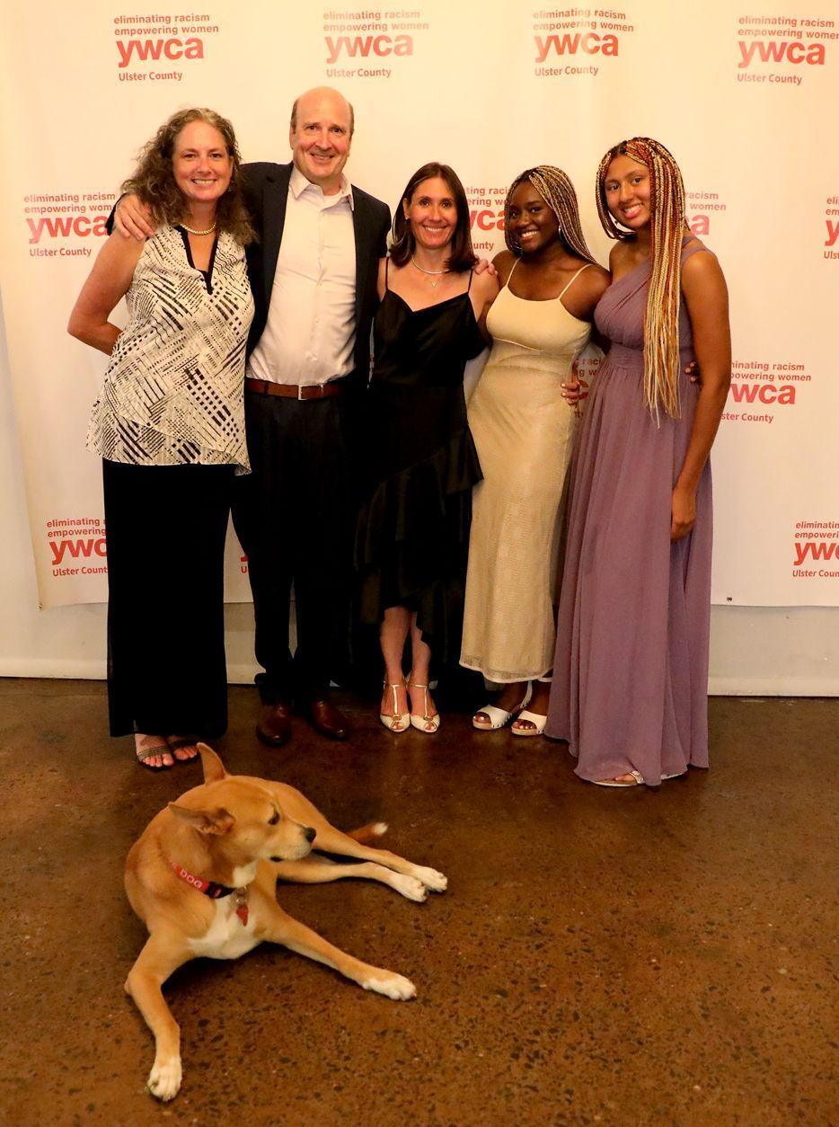Group of people smiling at an event, a dog rests on the floor in the foreground.