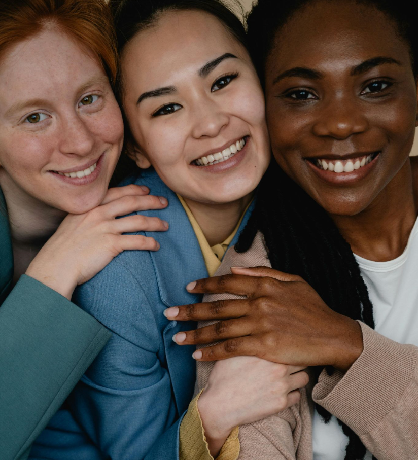 Three diverse women smiling and embracing.
