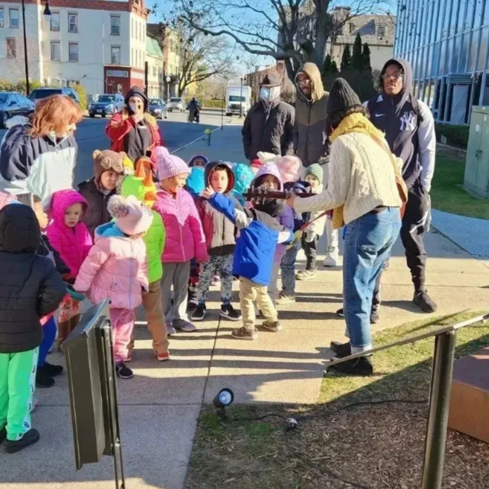 Children in colorful coats on a field trip, looking at a sculpture in front of a building.