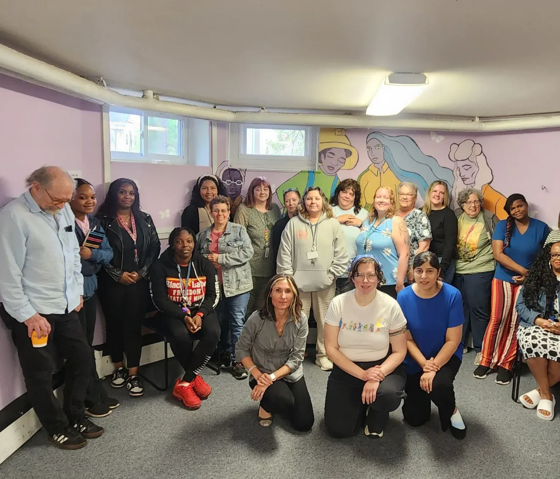 Group of diverse people posing for photo in a room with a mural.