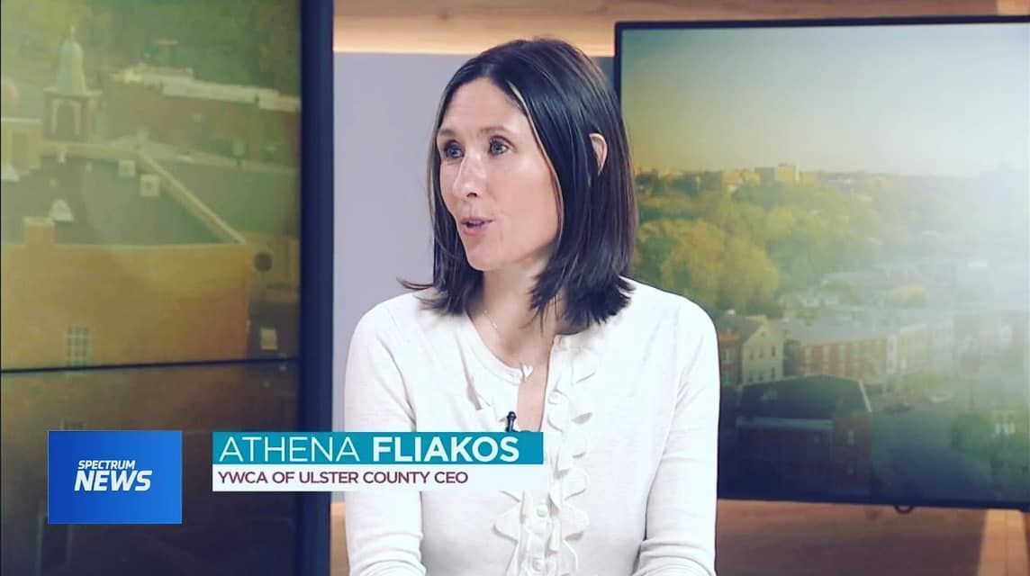 Athena Fliakos, YMCA of Westchester County CEO, in a TV interview. She wears a light sweater in a studio with a cityscape backdrop.