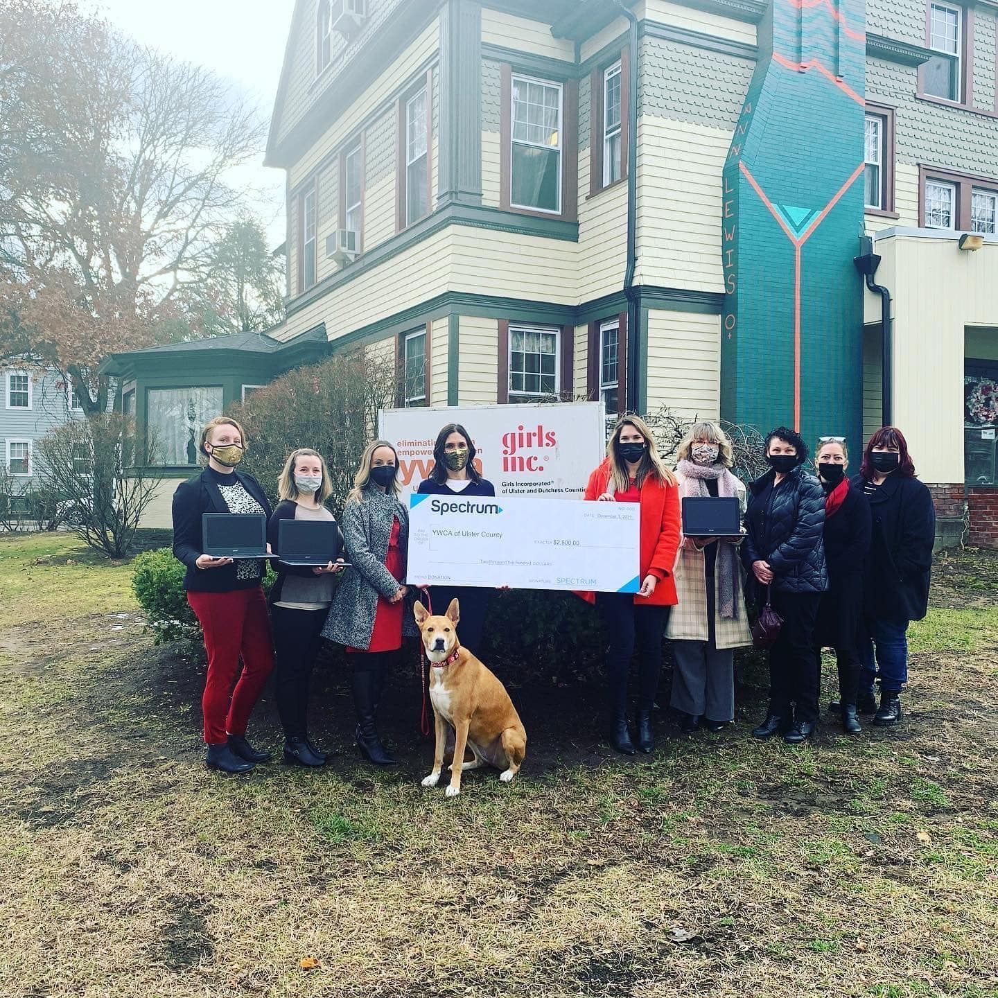 Group of women and a dog holding a large check in front of a building for Girls Inc.