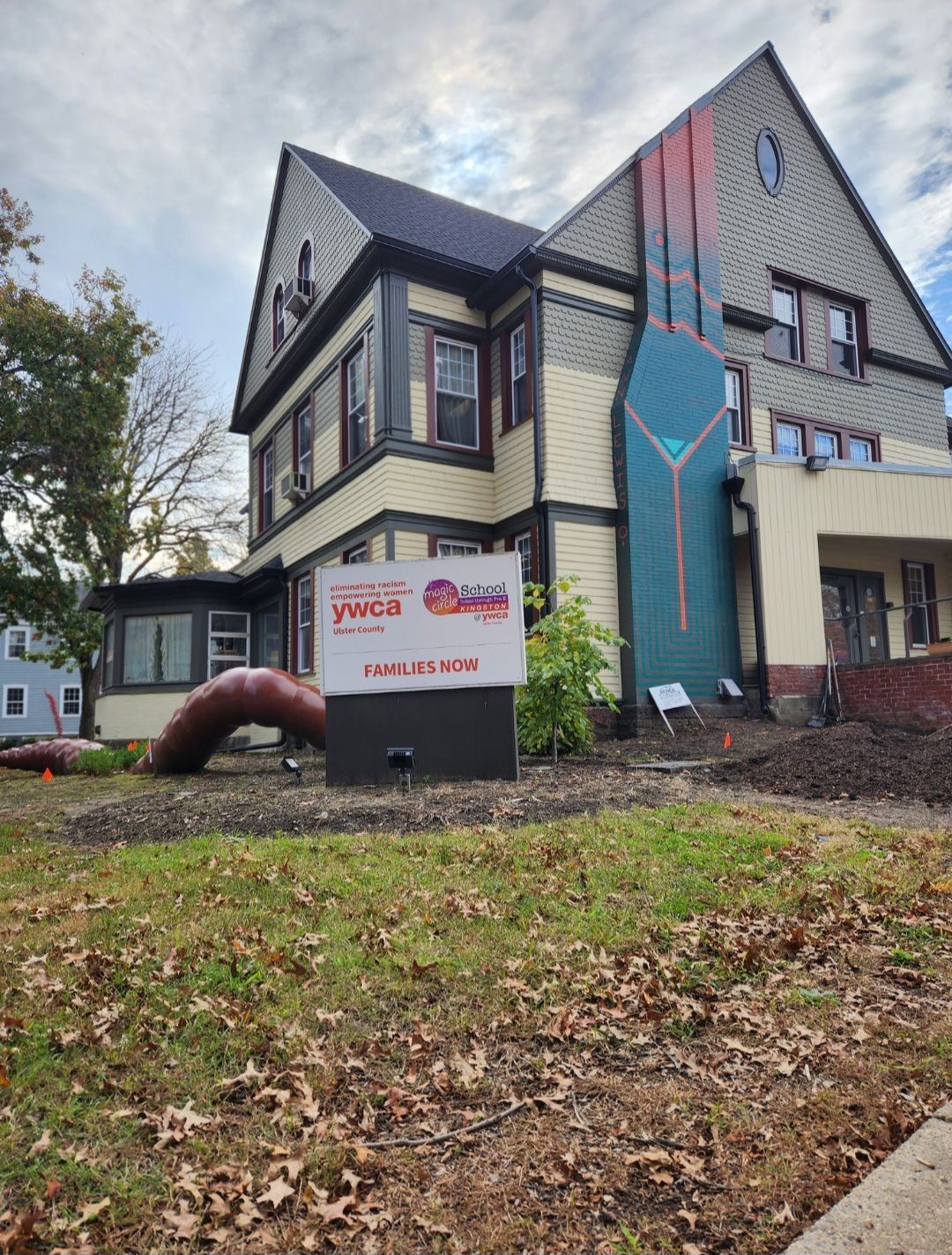 Exterior view of YMCA building with sign, chimney mural, and fall foliage.