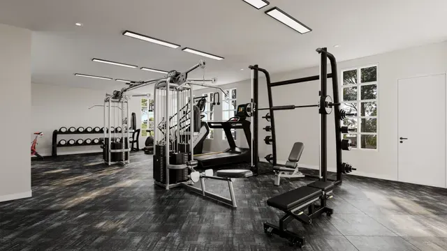 Gym interior with weight machines, a squat rack, and dumbbells. Dark floor, white walls, and bright lights.