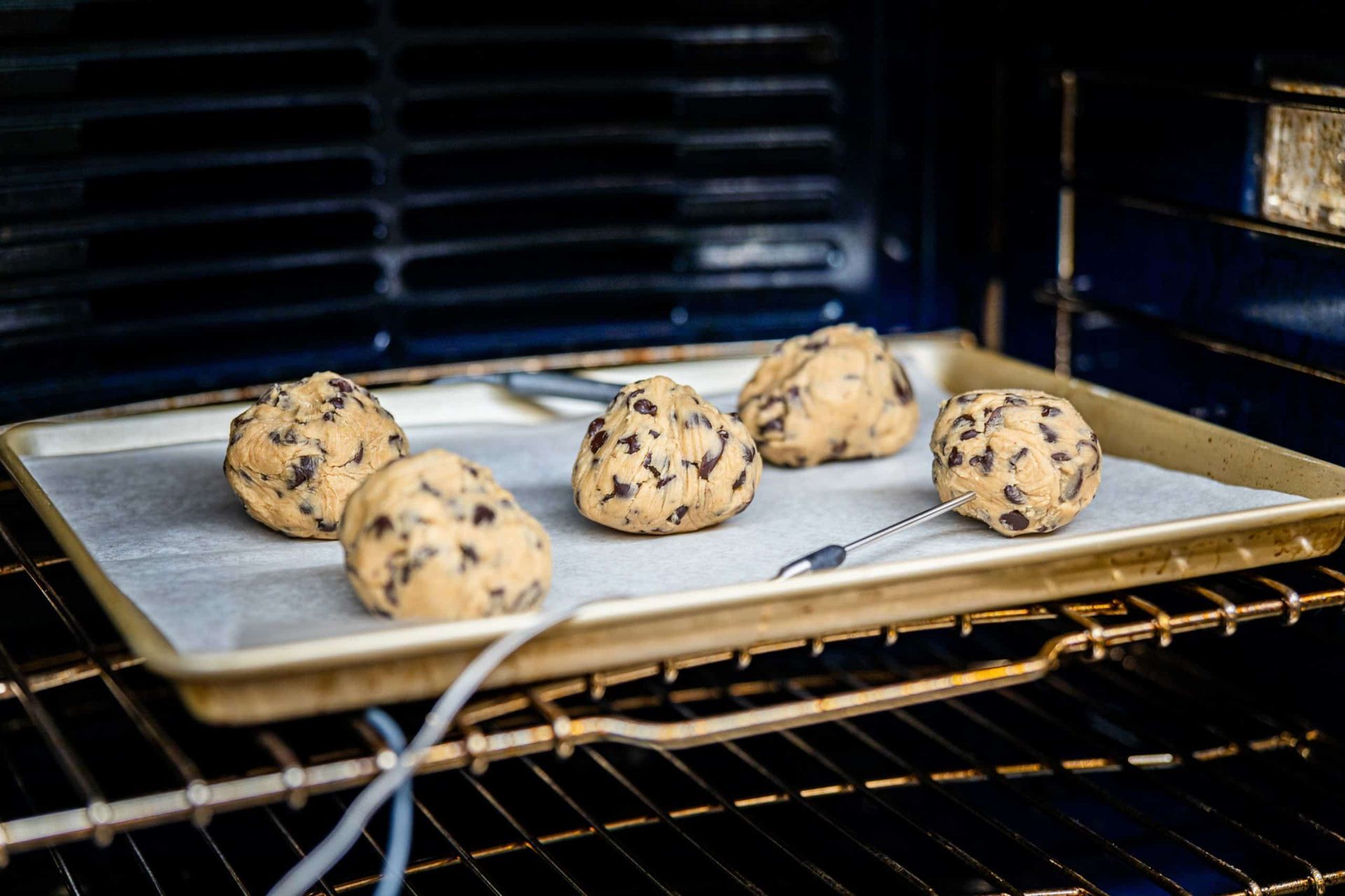 Chocolate chip cookie dough balls on a baking sheet in an oven.