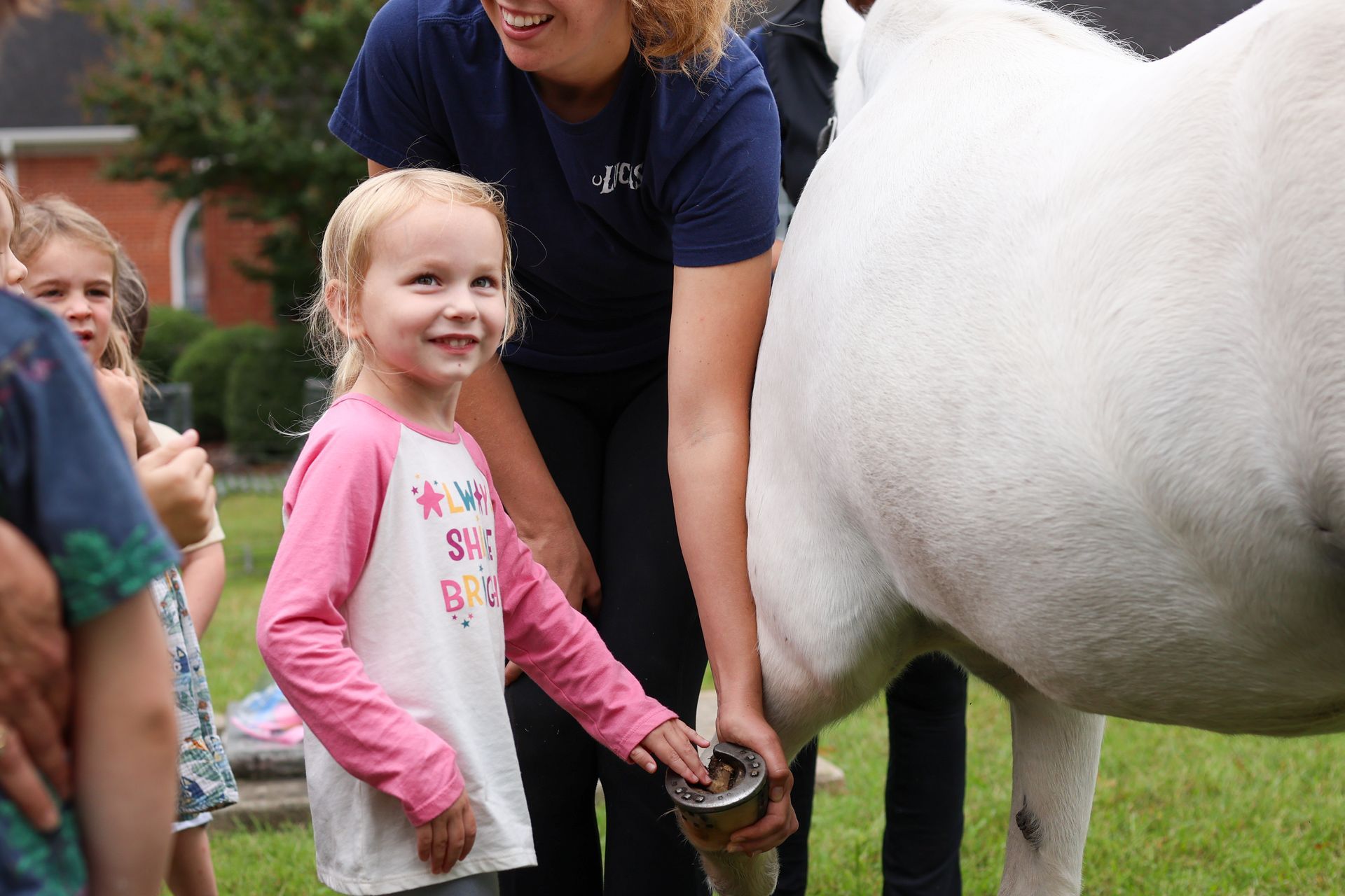 a girl smiling looking at the camera while touching a horse