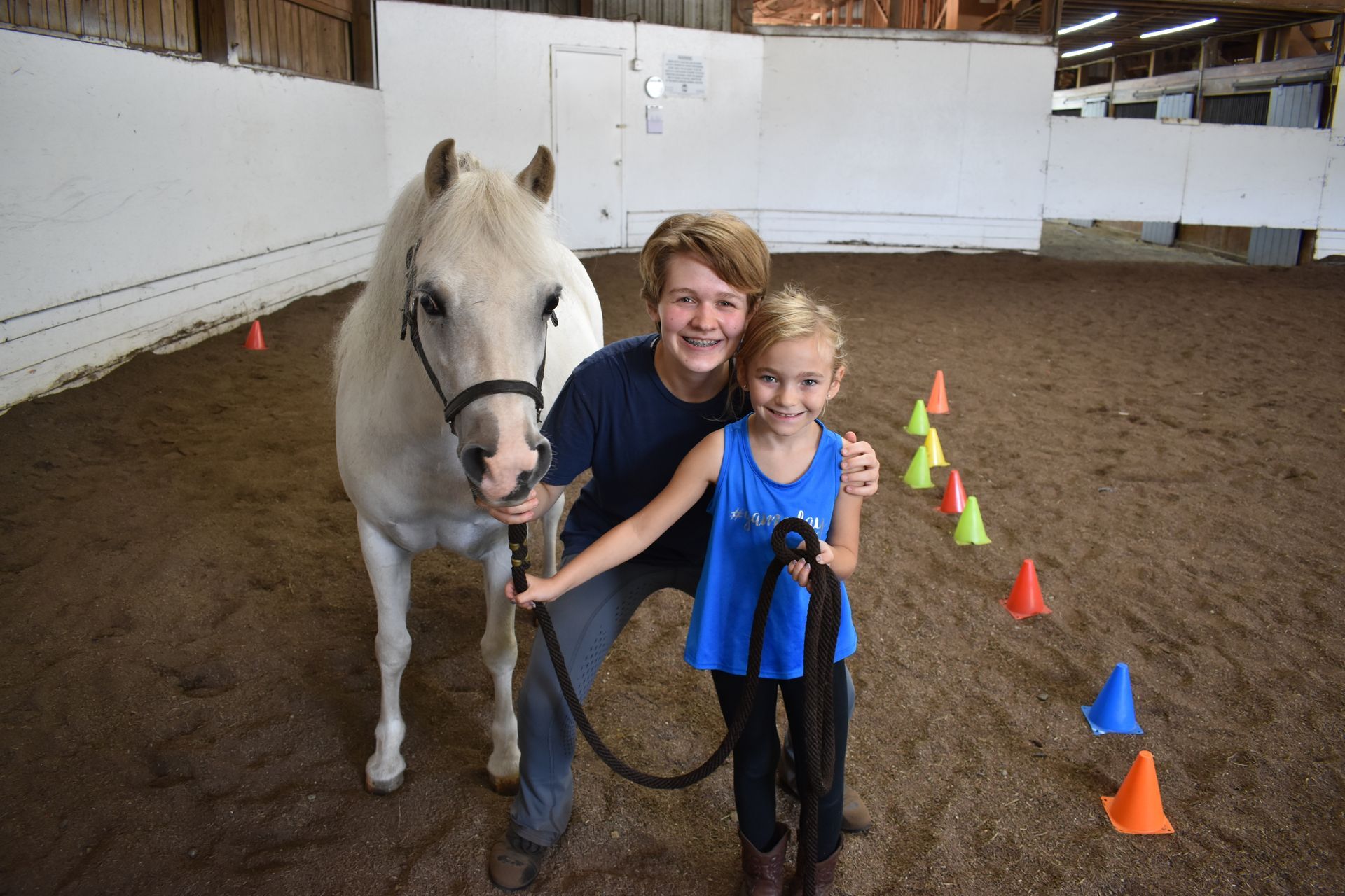 a teenager and a child next to a white horse inside the stable