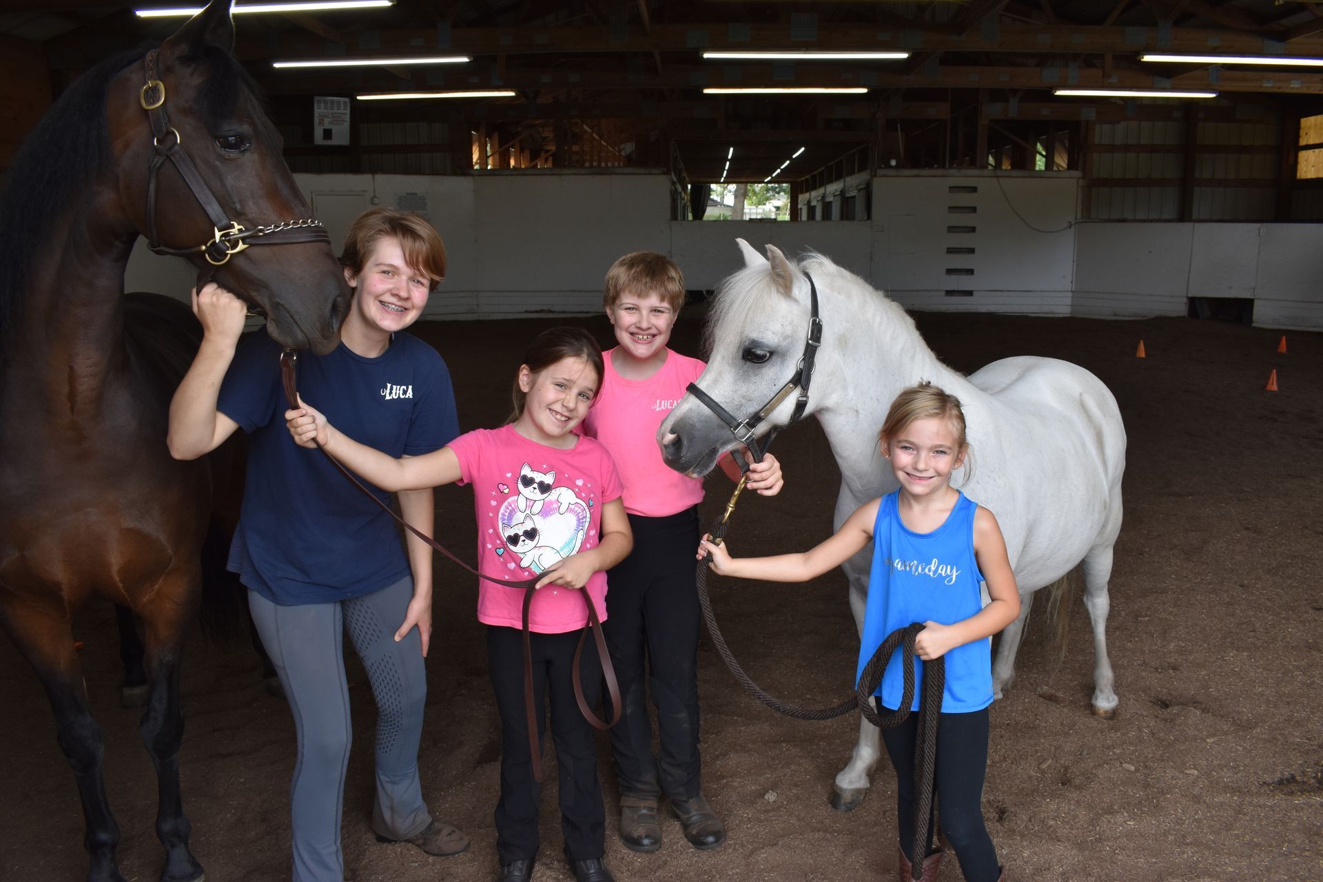 a teenager and 3 children holding 2 horses and smiling