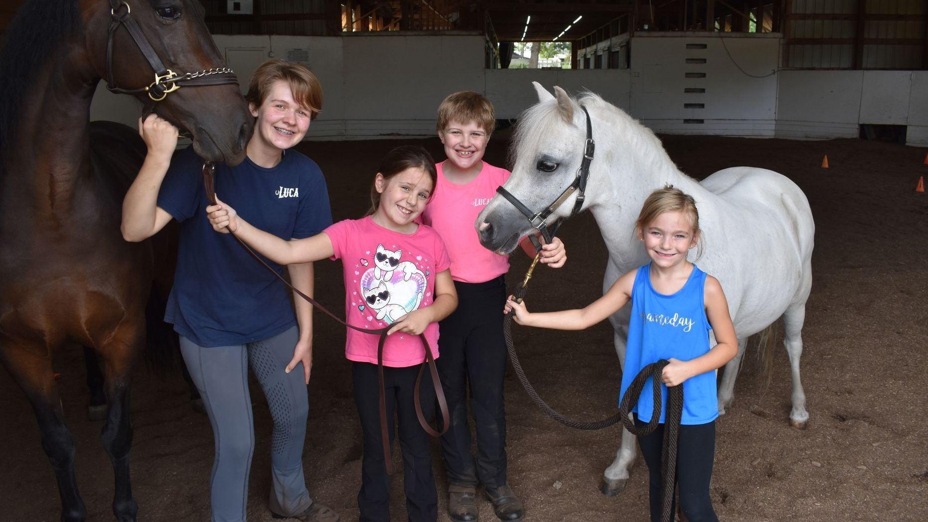 a group of children holding the reigns of two horses inside a stable