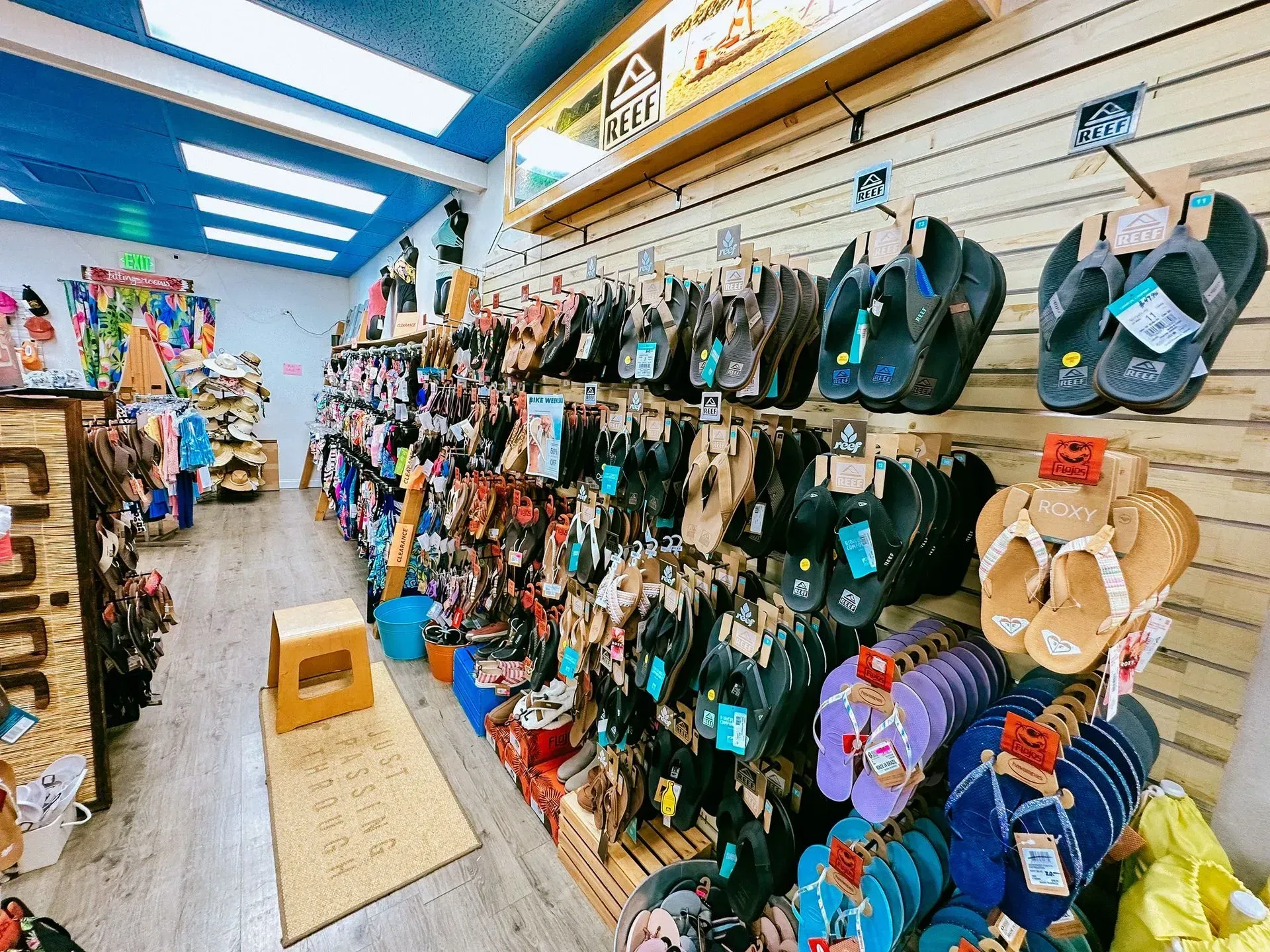 Shoe store interior with numerous flip-flops on display. Shelves, blue ceiling, and wooden accents.