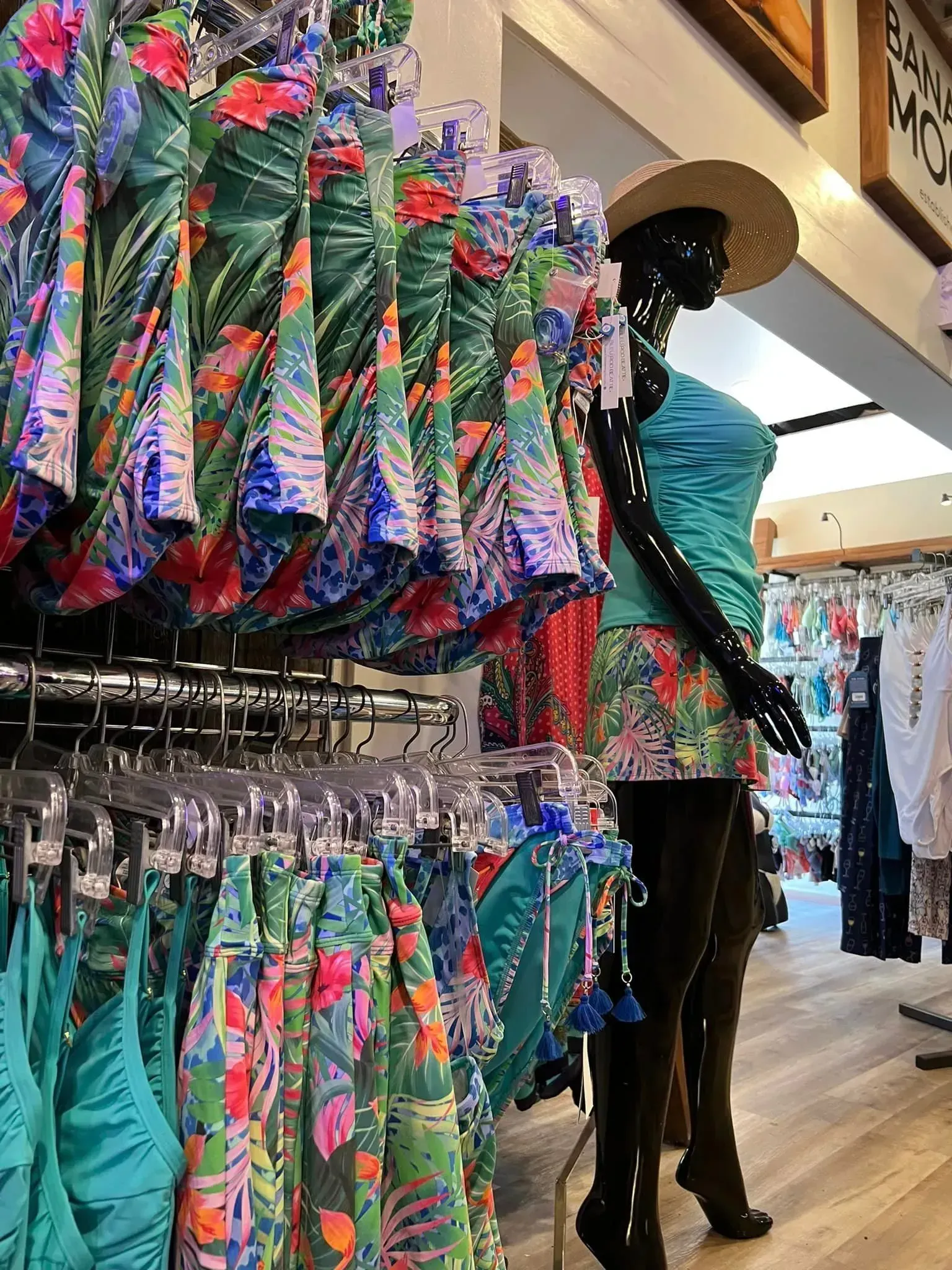 Swimwear display in a store. Mannequin wearing teal tank and skirt; printed swimwear hangs on racks.