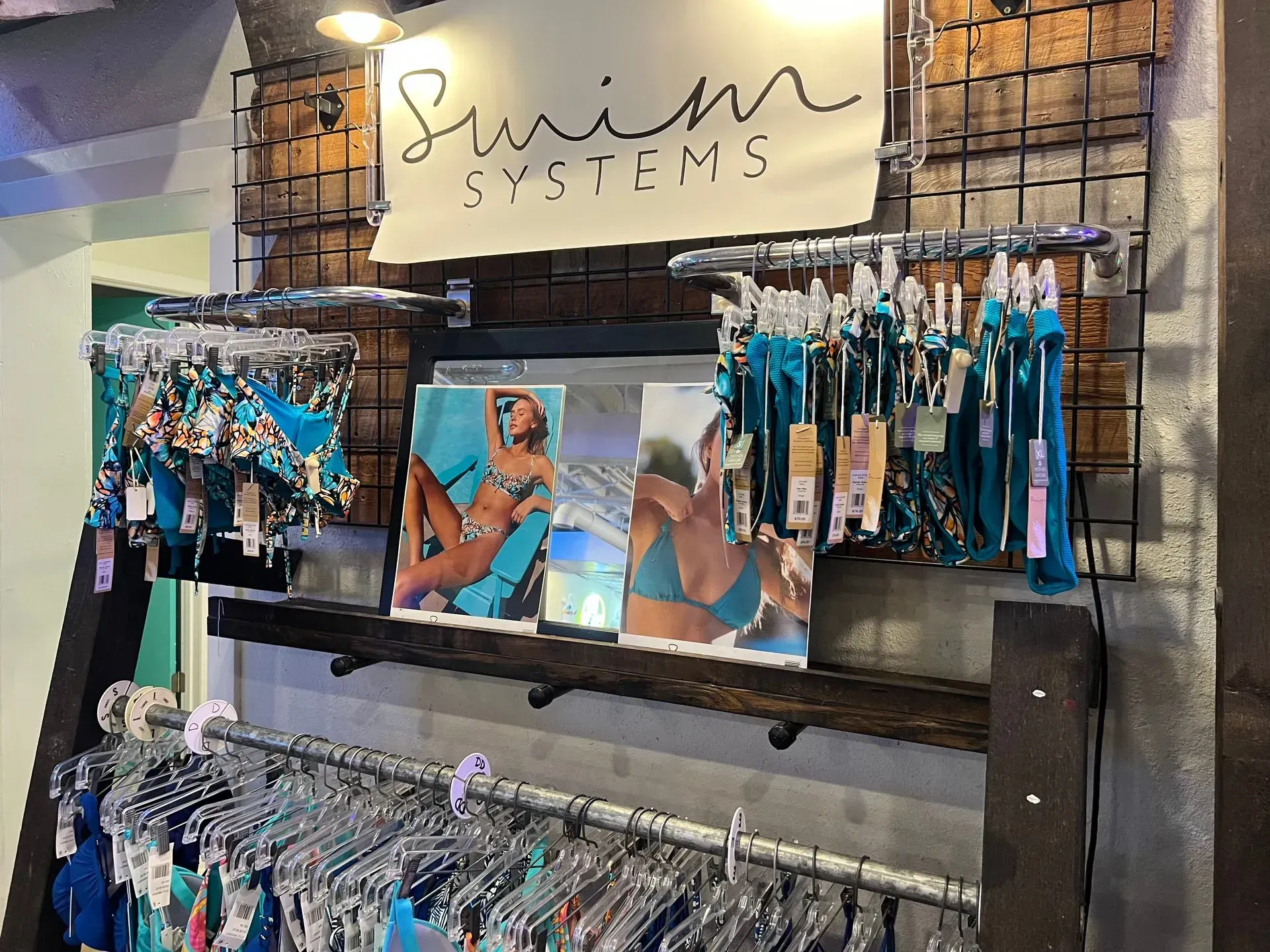 Swim Systems swimwear display: bikinis on hangers, posters, logo, turquoise hues.