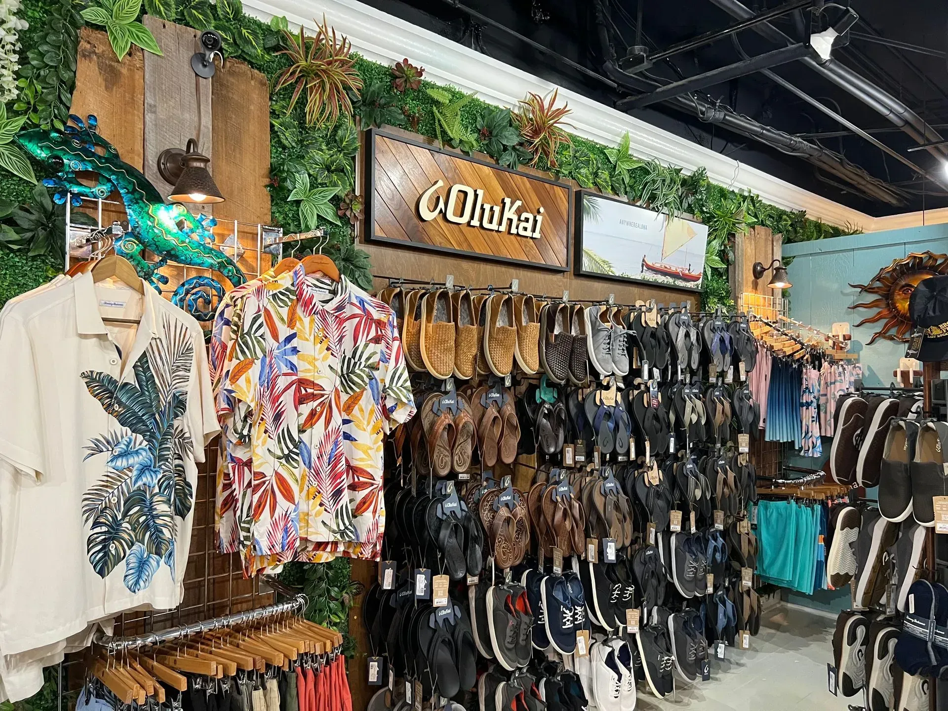 Inside a clothing store, Olukai apparel and footwear are displayed. A wall of sandals and shirts with tropical designs.