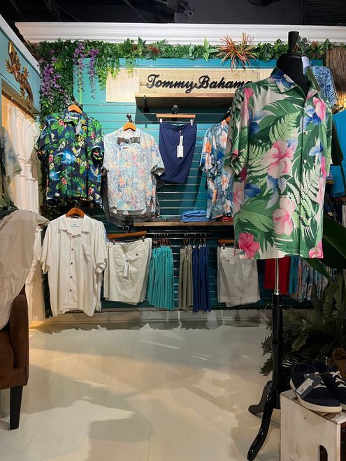 Clothing display in a Tommy Bahama store with shirts, pants, and a mannequin. Tropical theme with green, blue, and white colors.