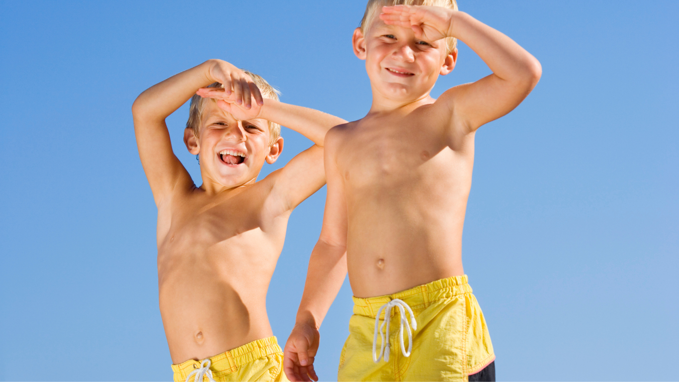 Two shirtless boys in yellow shorts shield eyes from the sun against a blue sky.