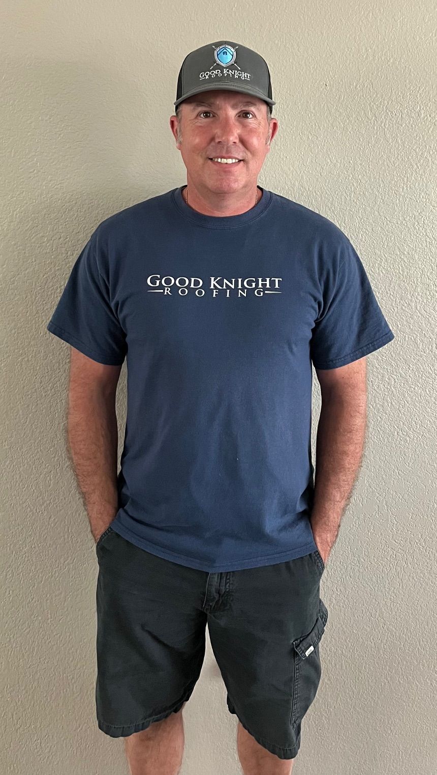 A man wearing a blue shirt and black shorts is standing with his hands in his pockets.