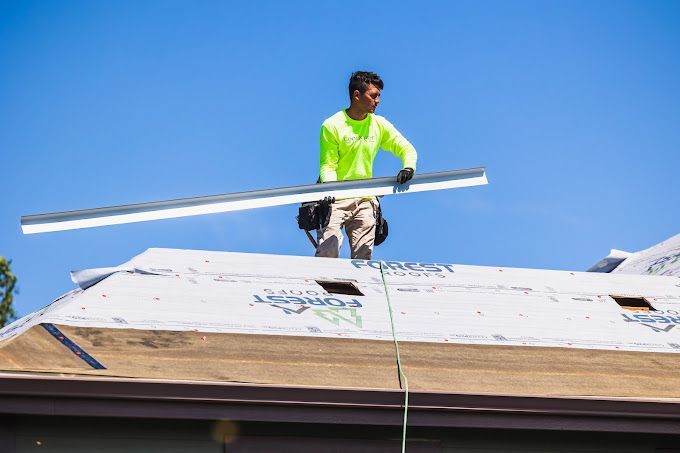 A man is standing on top of a roof holding a piece of metal