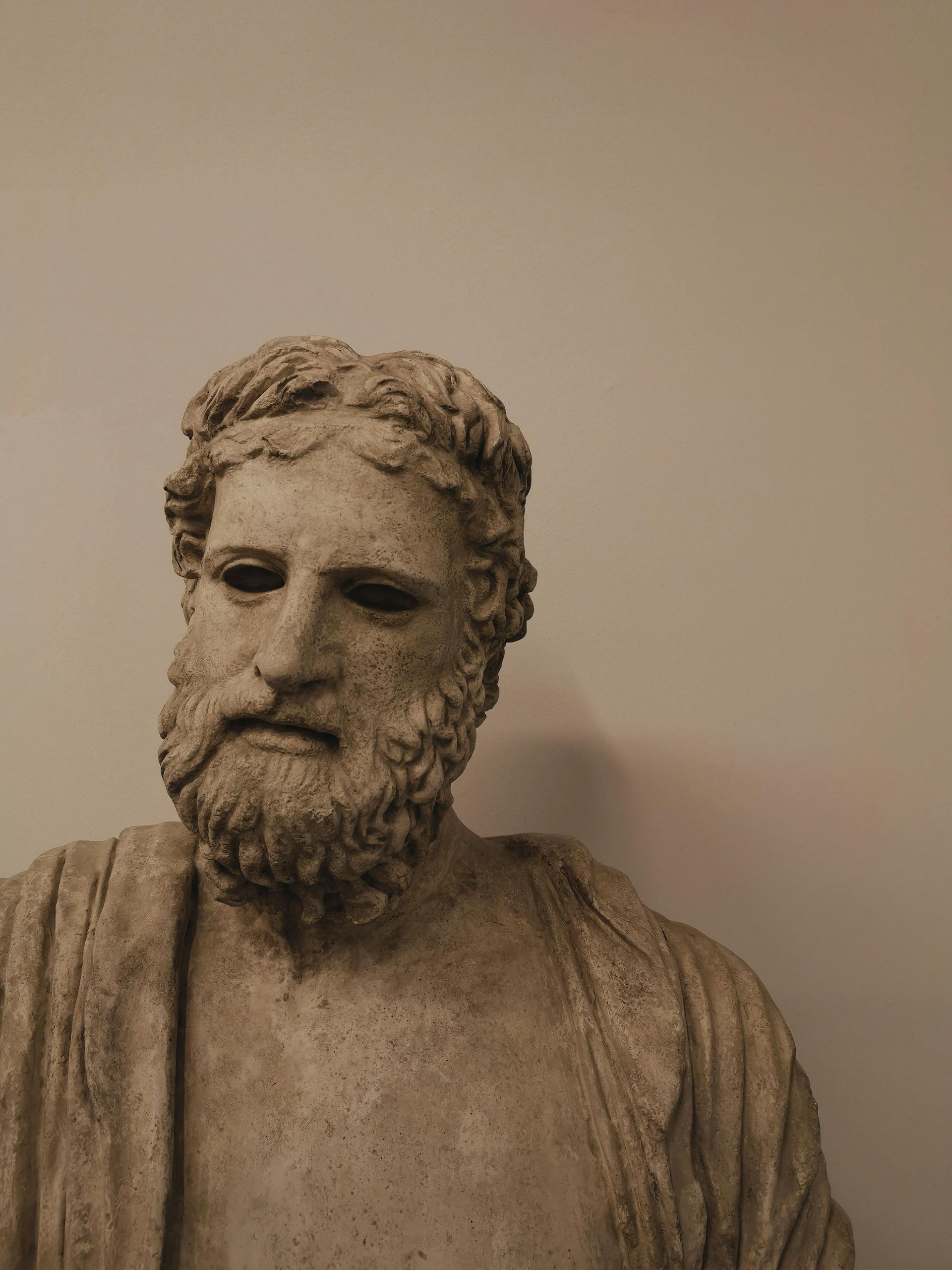 A statue of a man with a beard is against a white wall