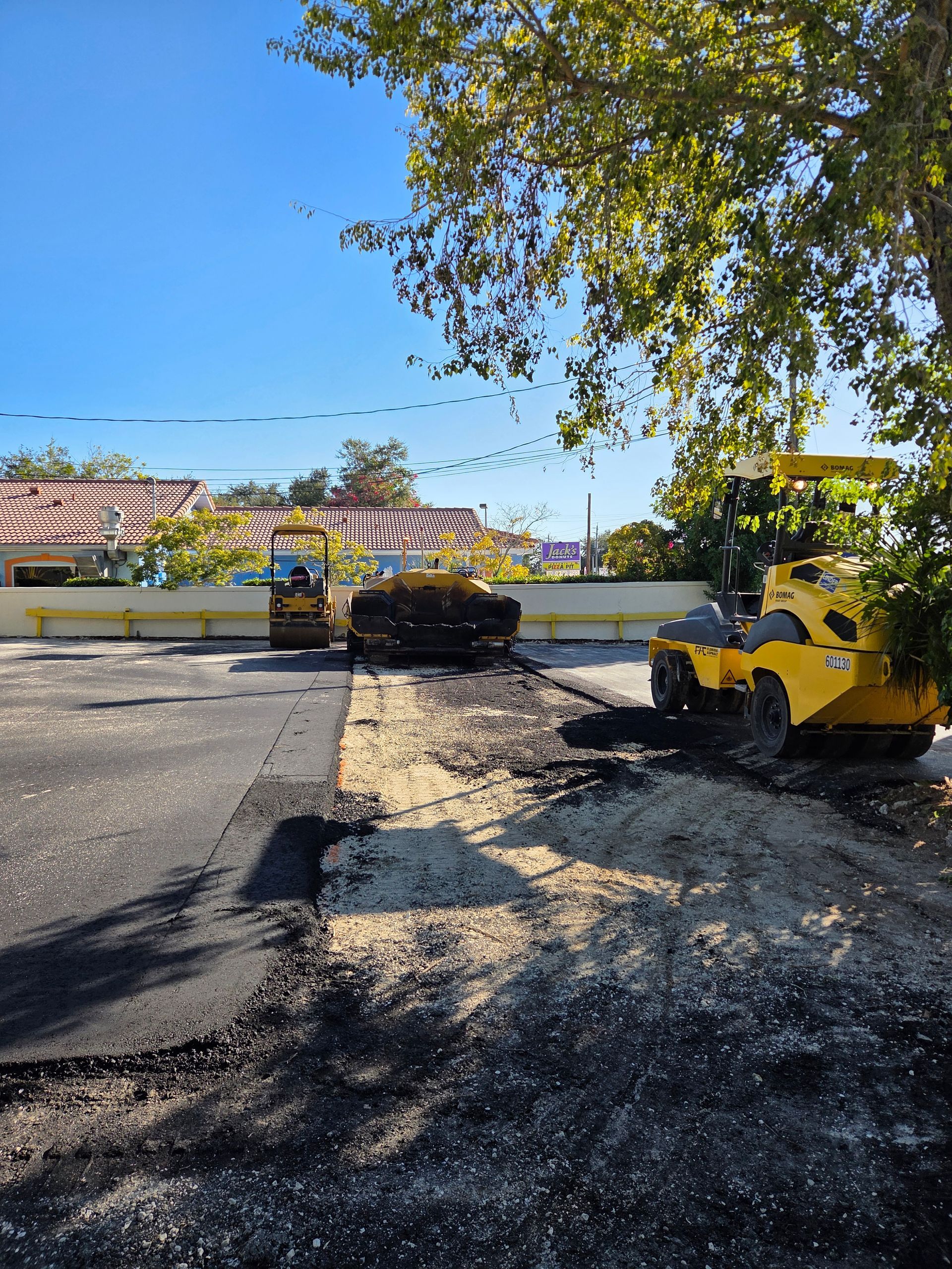 Asphalt paving in progress: two yellow compactors, freshly laid asphalt, gravel base, blue sky.