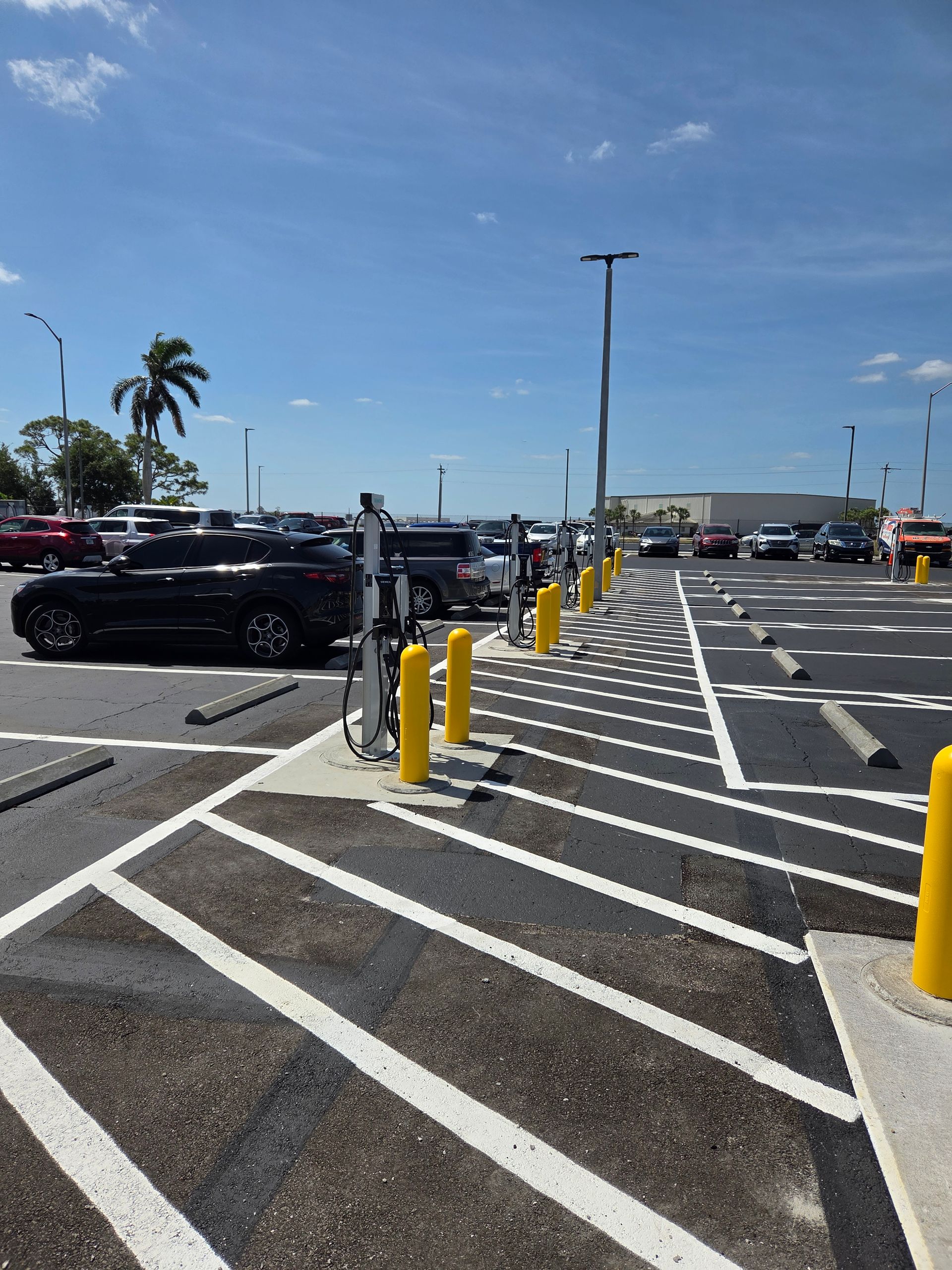 Parking lot with electric vehicle chargers, yellow posts, and striped parking spaces. Sunny day.