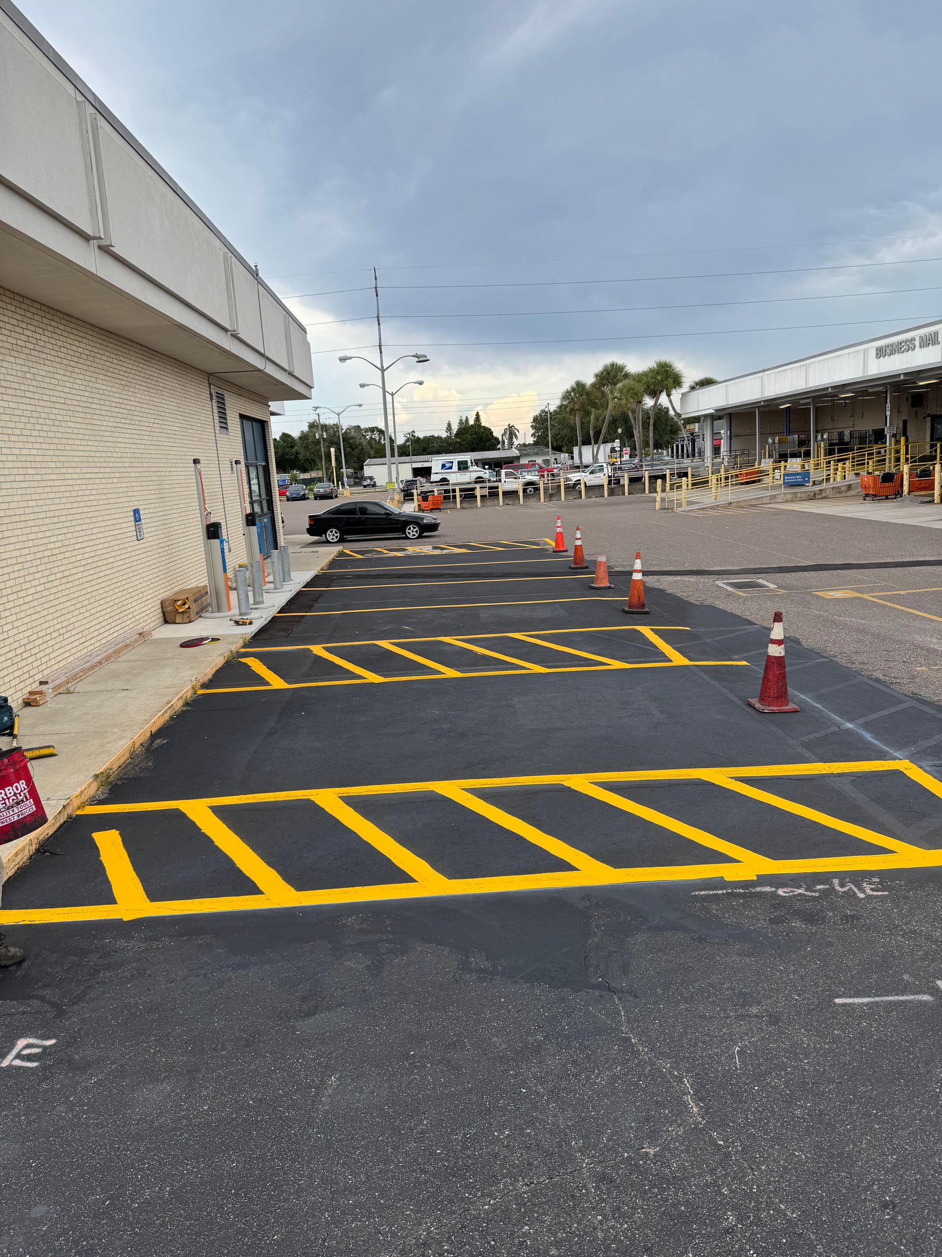 Exterior view of a building with fresh yellow parking lines on asphalt. Orange traffic cones stand near the lines.