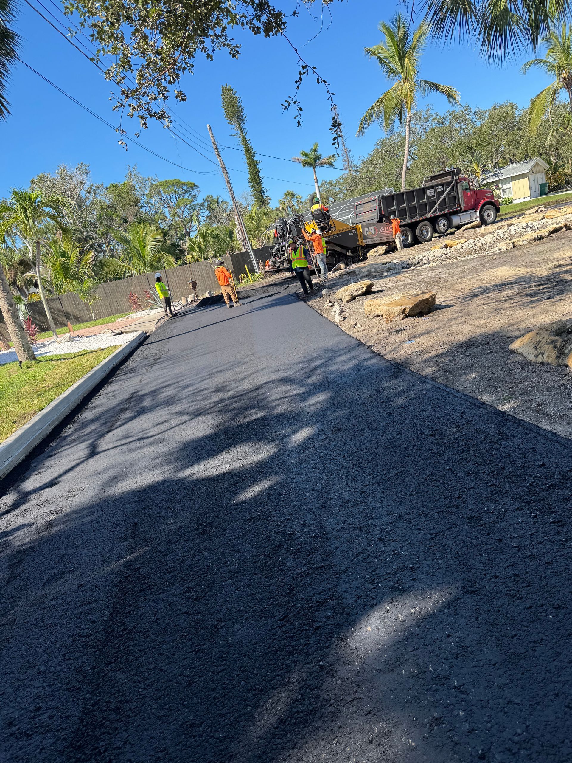 Road paving in progress. Workers in safety vests are laying asphalt on a sunny day.