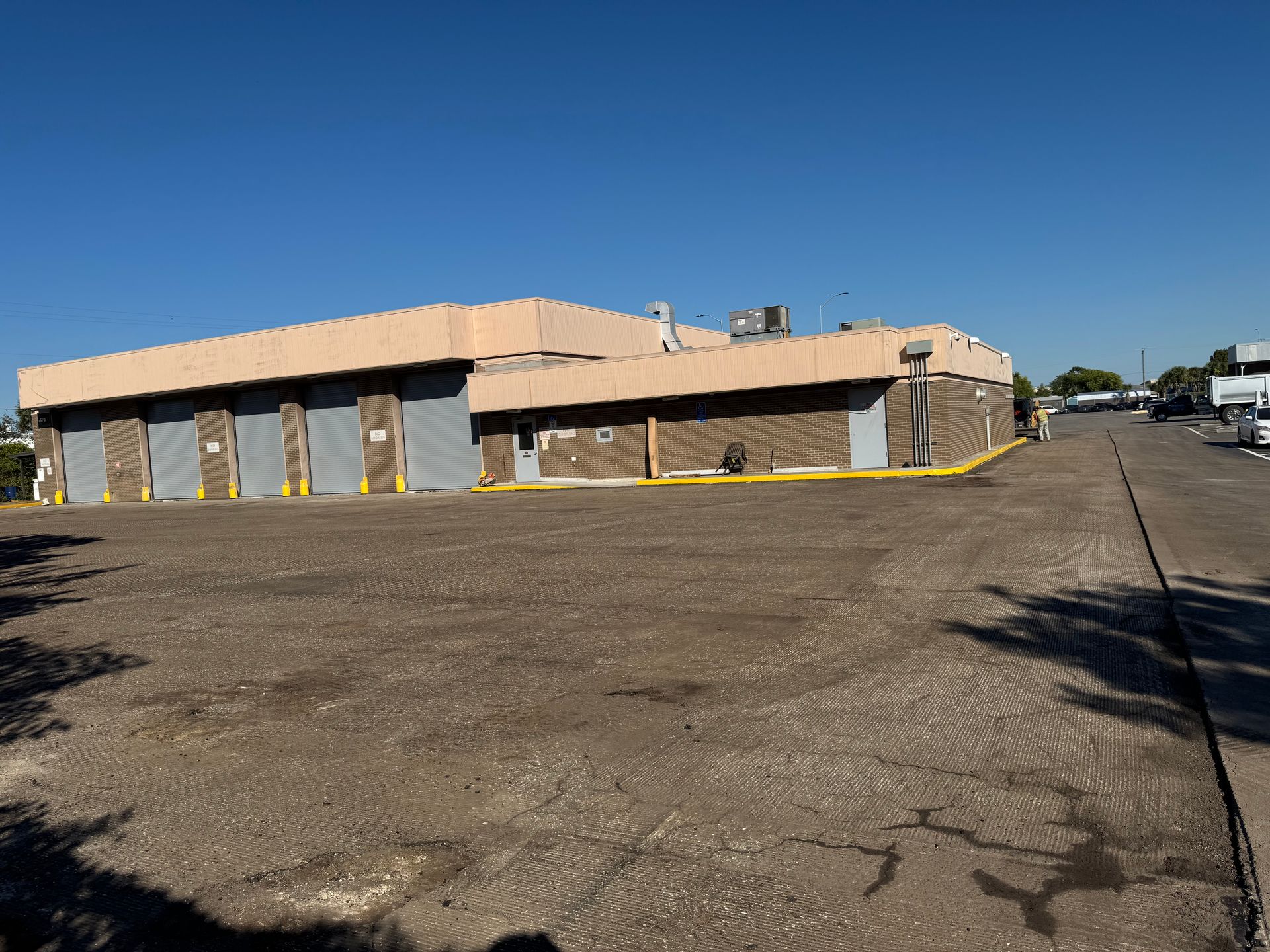 Industrial building with loading docks, tan trim, and paved area under a blue sky.