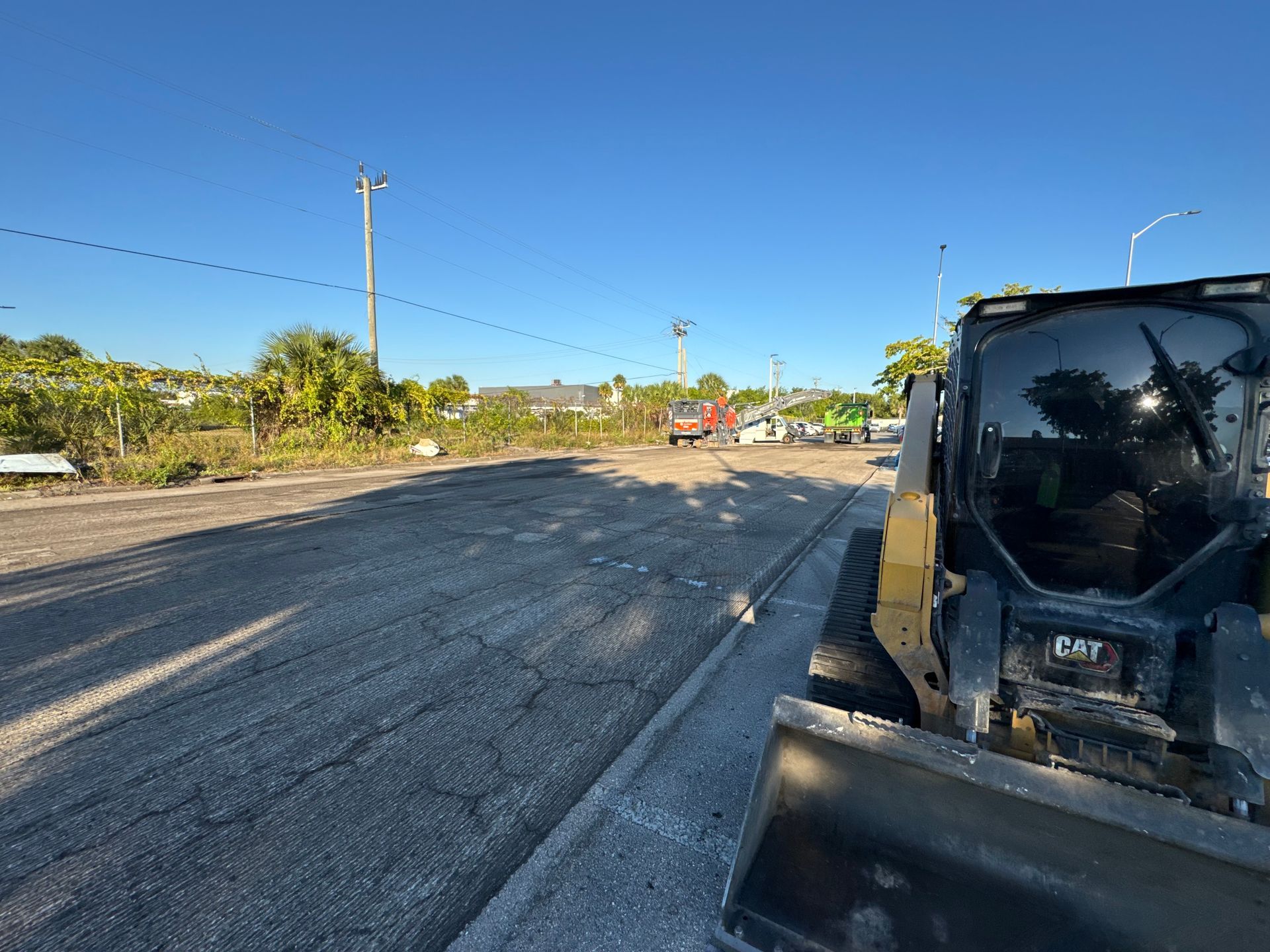 Construction site with a skid steer loader. Road work in progress with workers and vehicles visible. Sunny day.