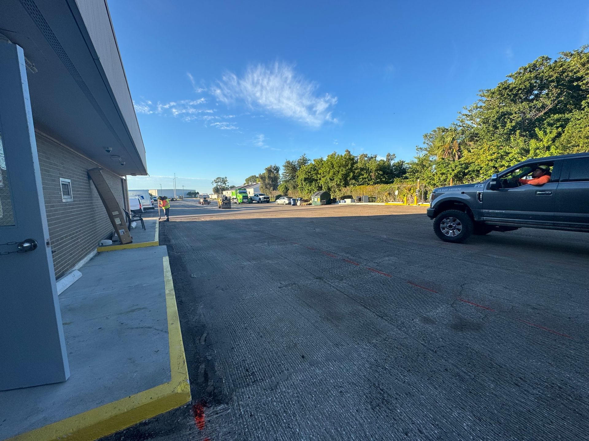 Exterior view of building with gravel parking lot, a truck, and workers under blue sky.