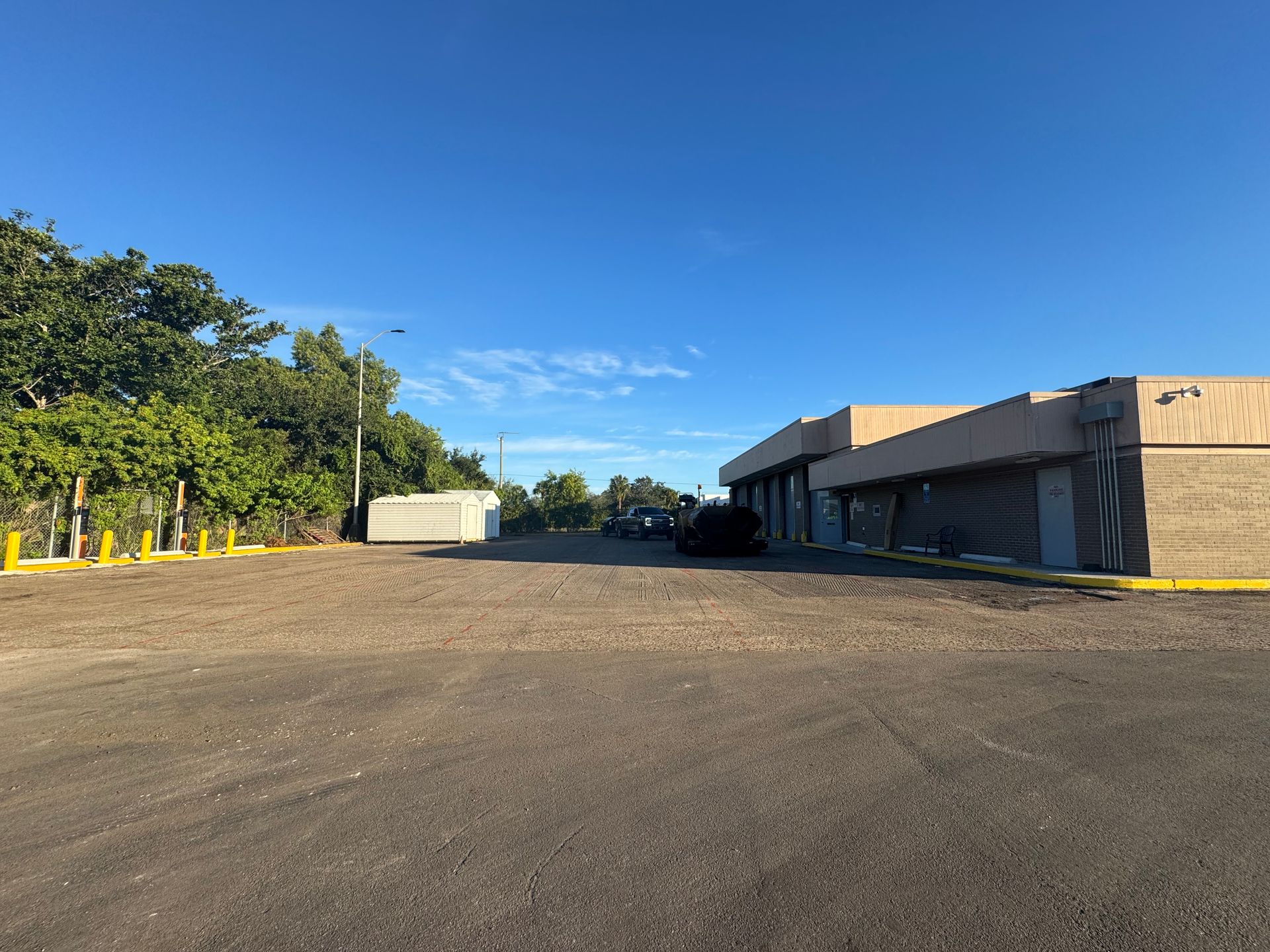 Large parking lot with trees and a low, rectangular building under a clear blue sky.