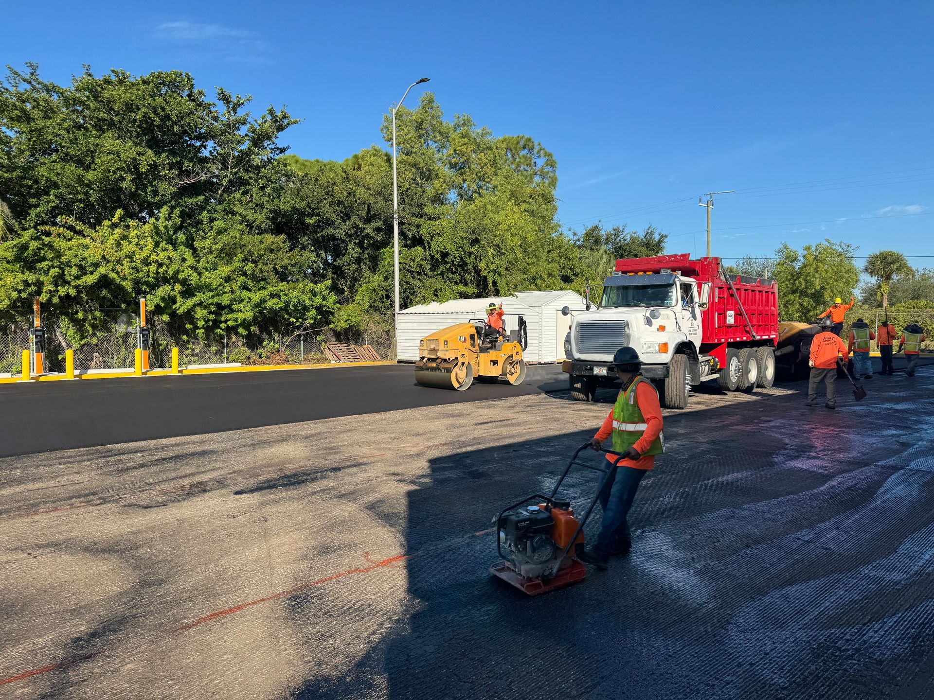 Road construction: Workers laying asphalt with machinery and truck on a sunny day.