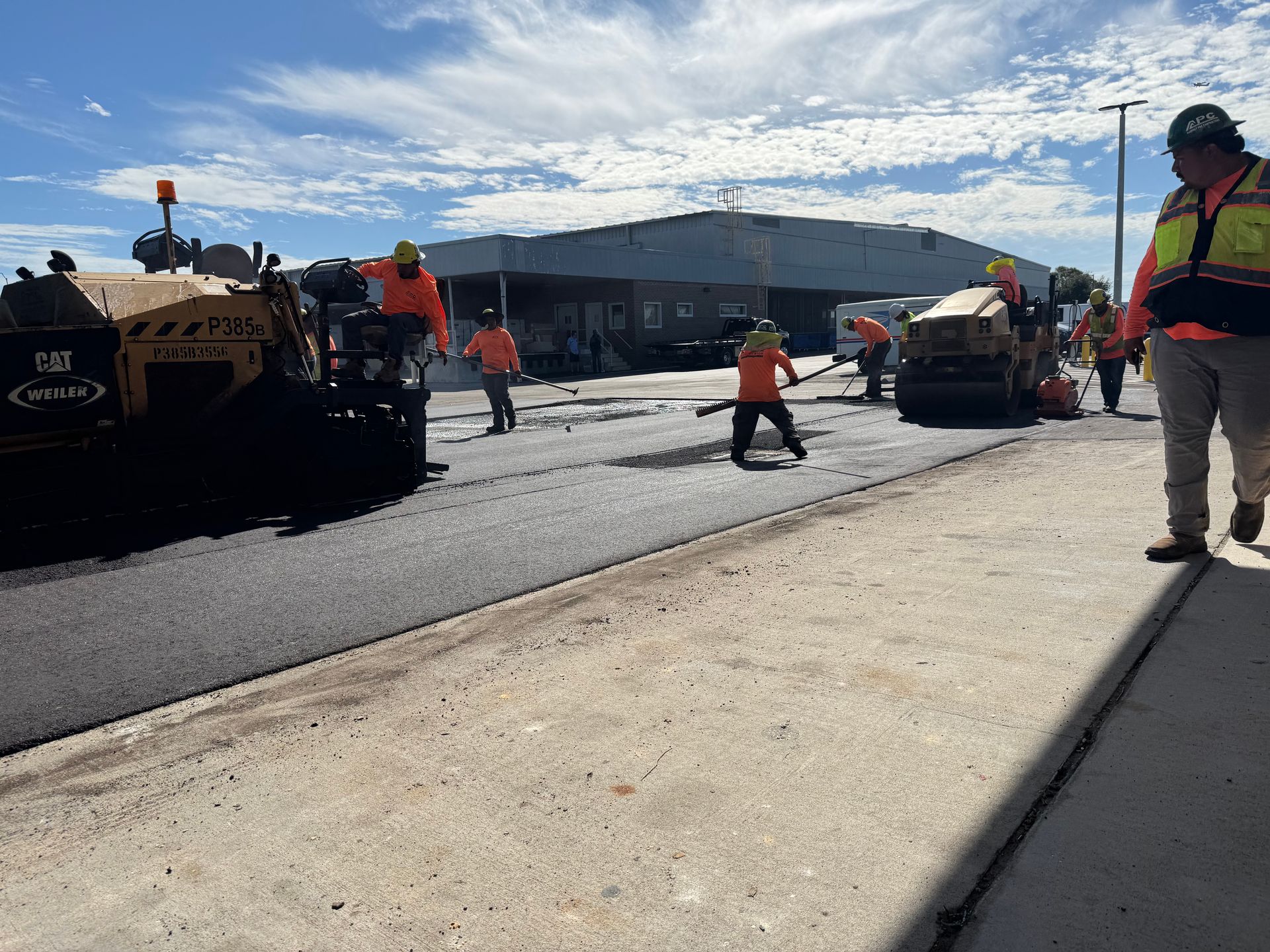 Road construction: workers laying asphalt with machinery and tools on a sunny day.