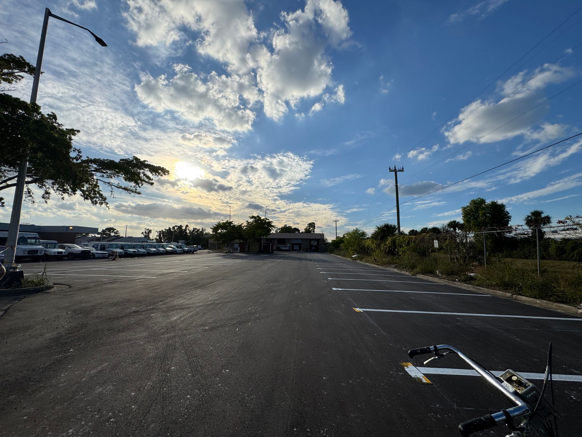 Wide shot of asphalt parking lot under a cloudy blue sky, with a bicycle in the foreground.
