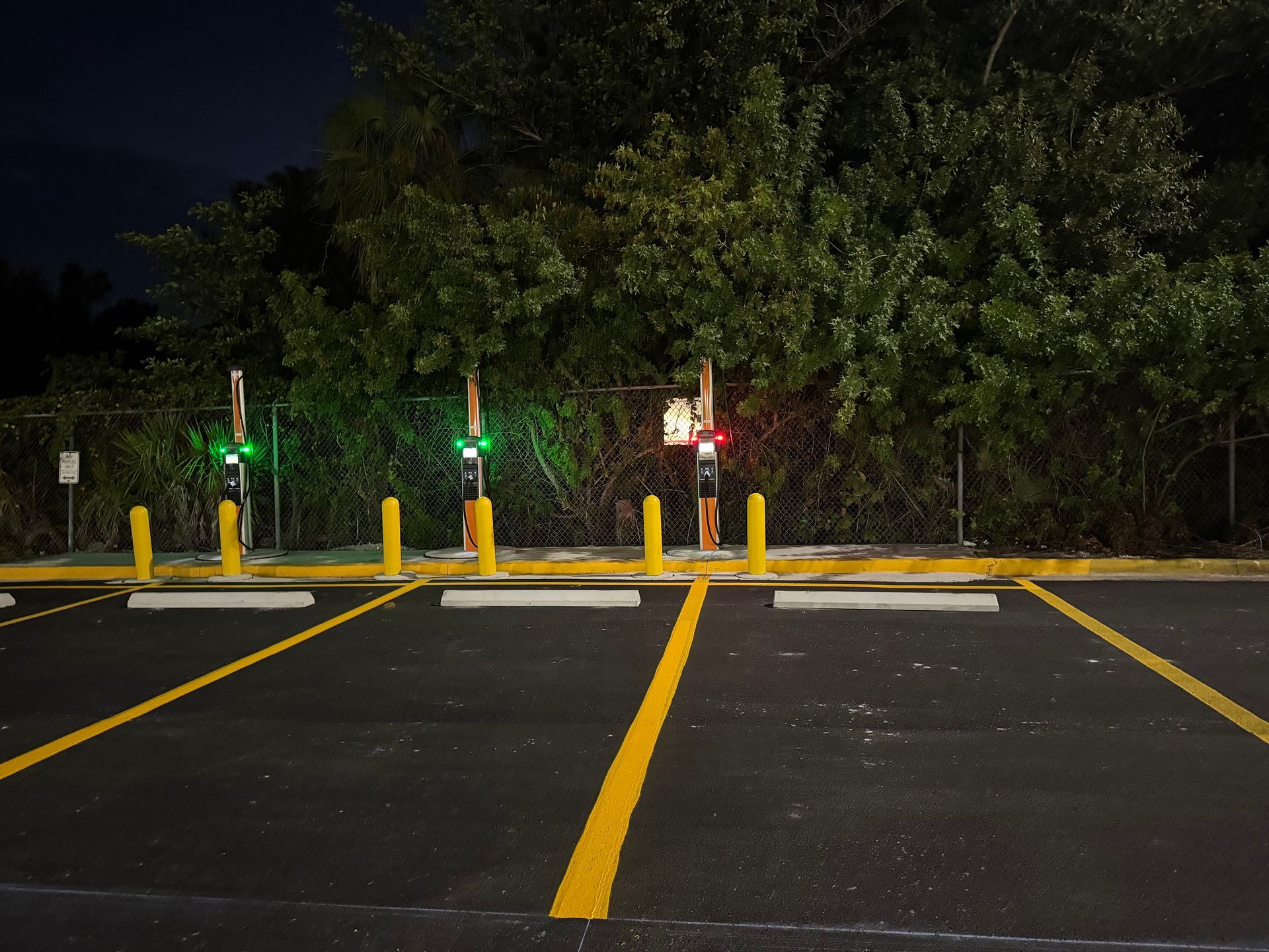 Electric vehicle charging station with illuminated indicators; two green, one red. Empty parking spaces. Dark night.
