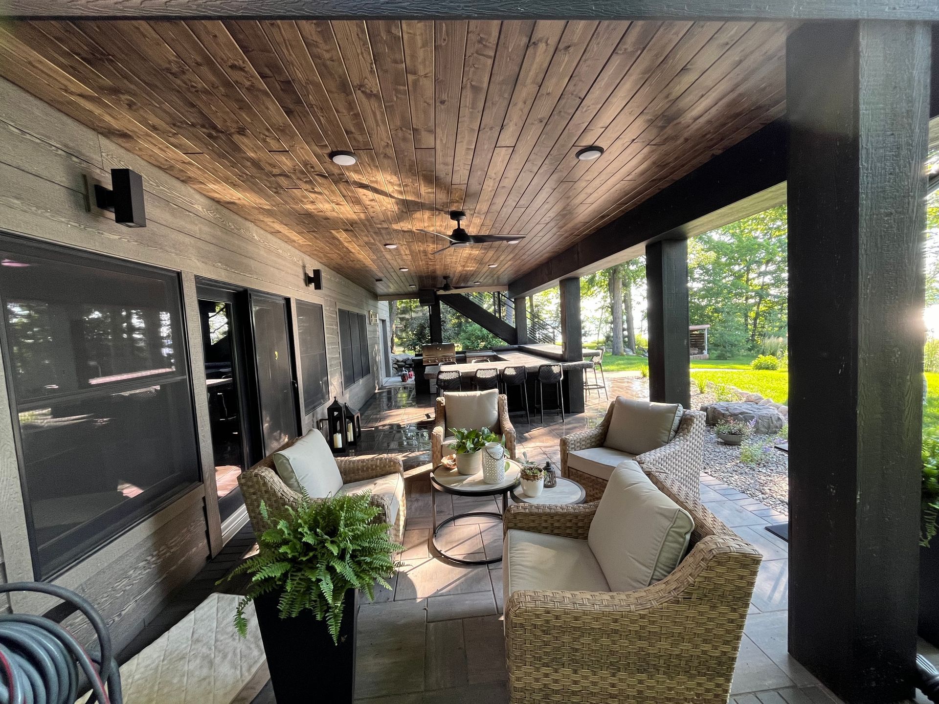 Covered patio with wicker furniture, dining table, and dark wood ceiling.