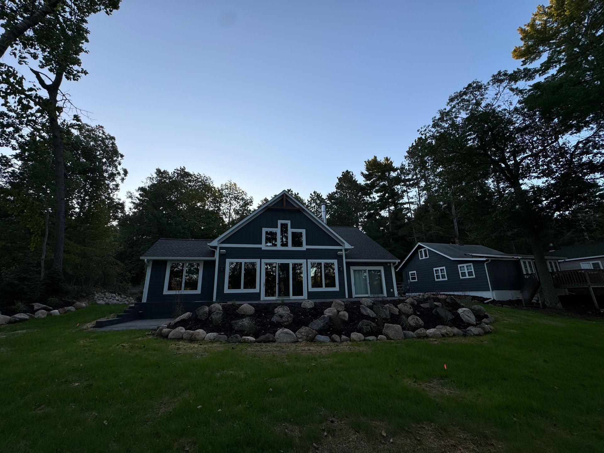 Dark blue house with multiple windows surrounded by trees and a grassy lawn.