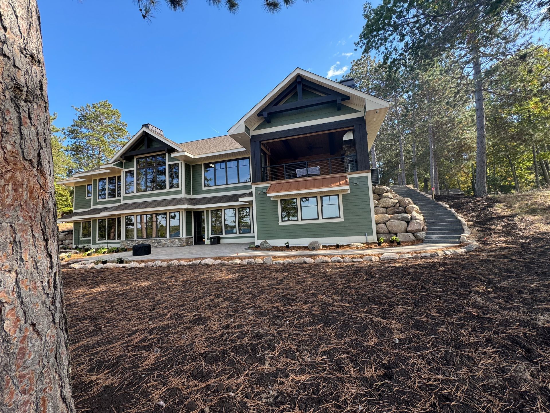 Green house with many windows sits among trees and dark mulch on a sunny day.