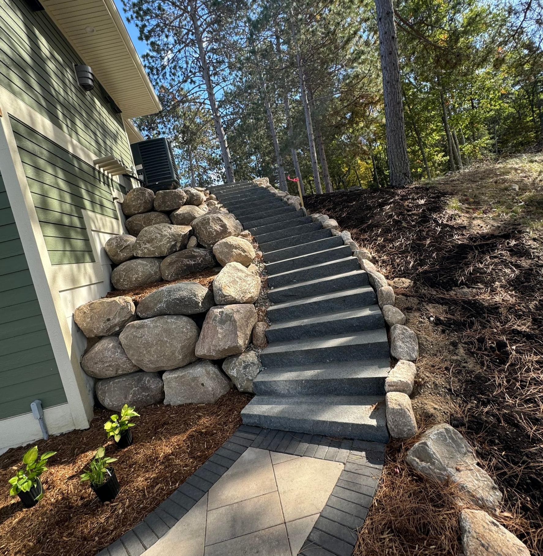 Stone steps ascend a hillside, flanked by a rock retaining wall and trees.