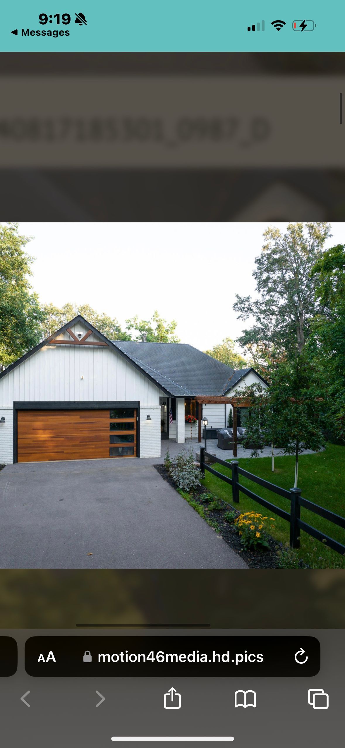 A white house with a brown garage door, dark driveway, and black fence.