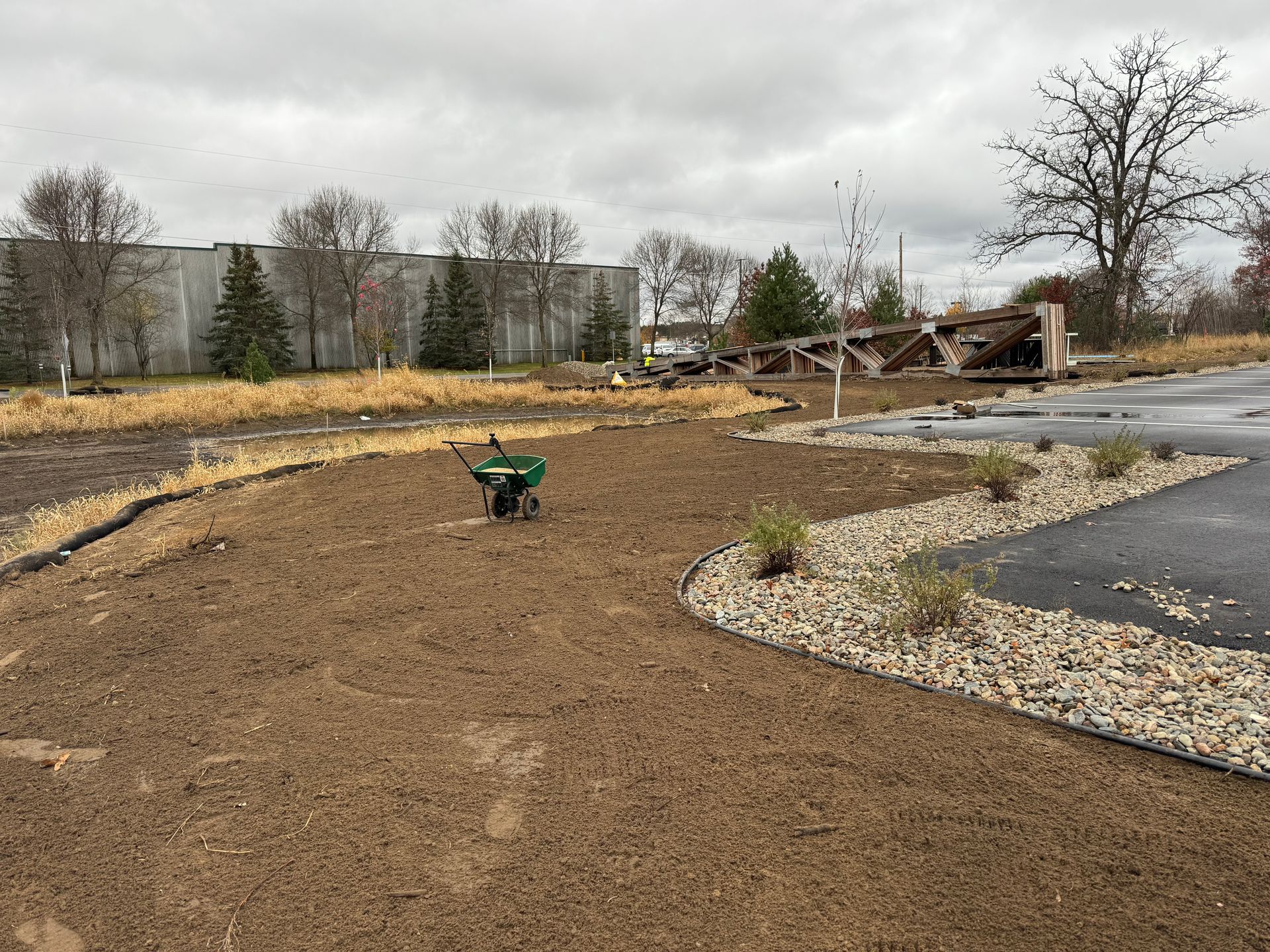 New landscaping with mulch and rocks, wheelbarrow in the middle, industrial buildings in the background.