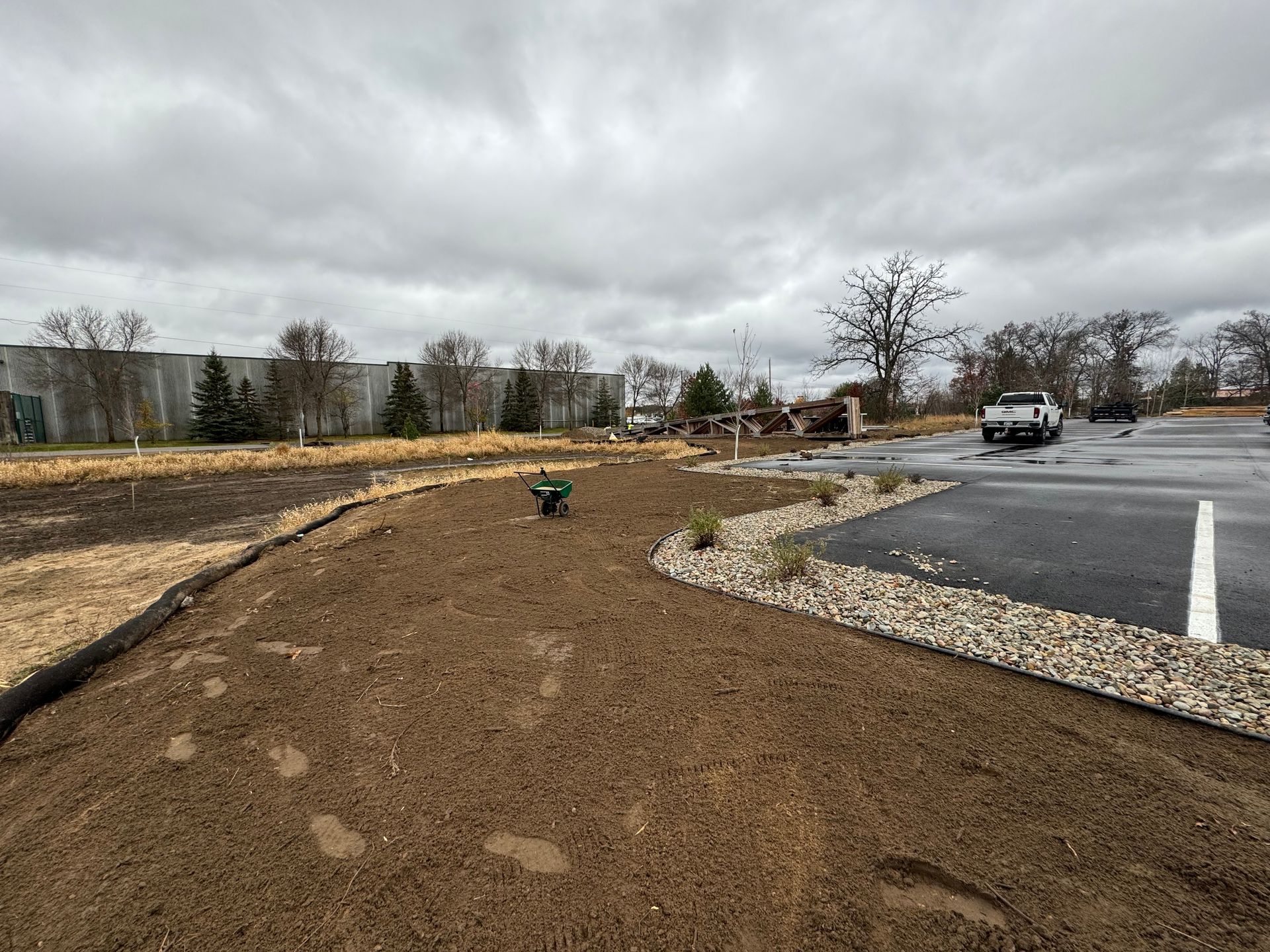 A construction site with a freshly tilled brown soil area, bordered by gravel and black fabric.