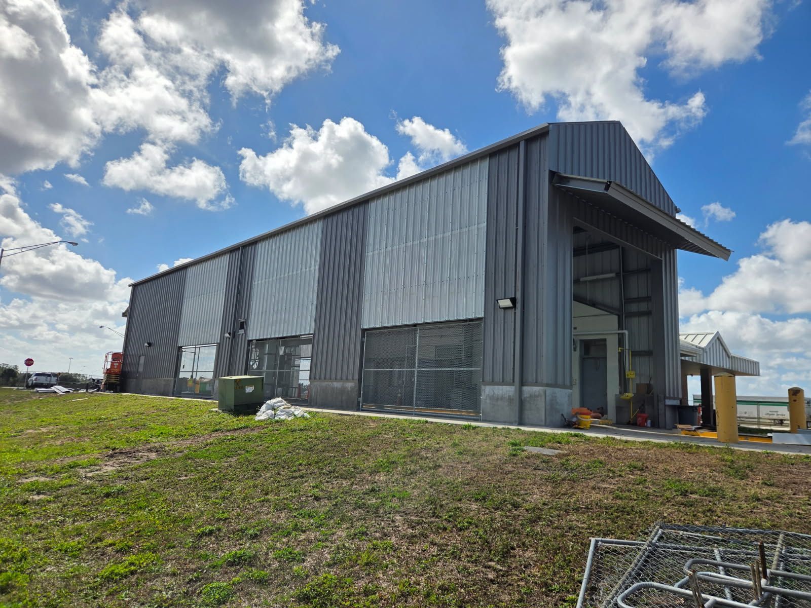 Metal industrial building with open bay doors under a cloudy sky.