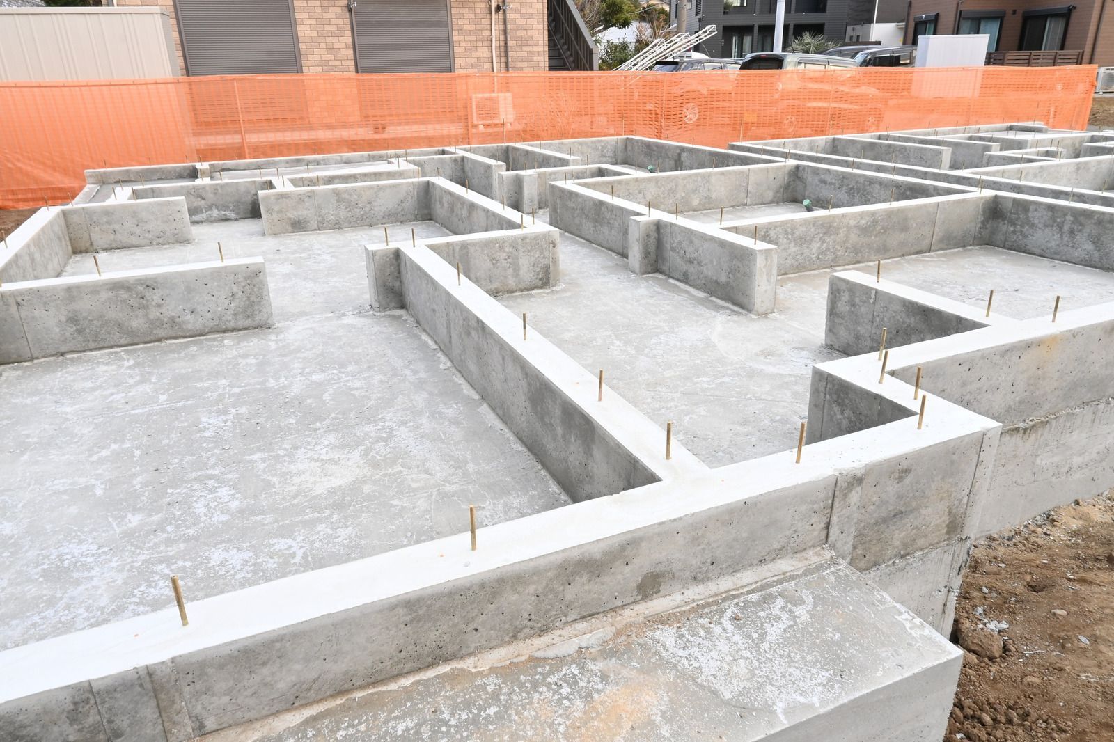Concrete foundation for a building under construction, with exposed framework and orange safety fencing.