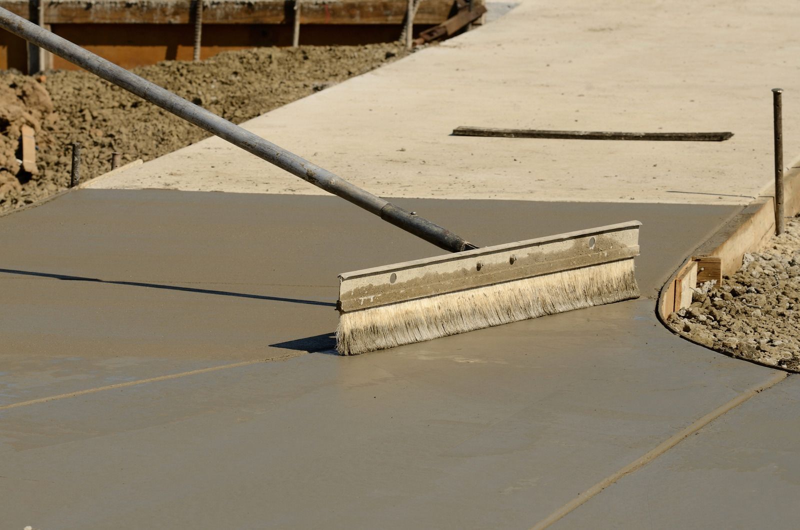 Leveling wet concrete with a screed tool. Gray concrete, wooden forms, and a long-handled tool.