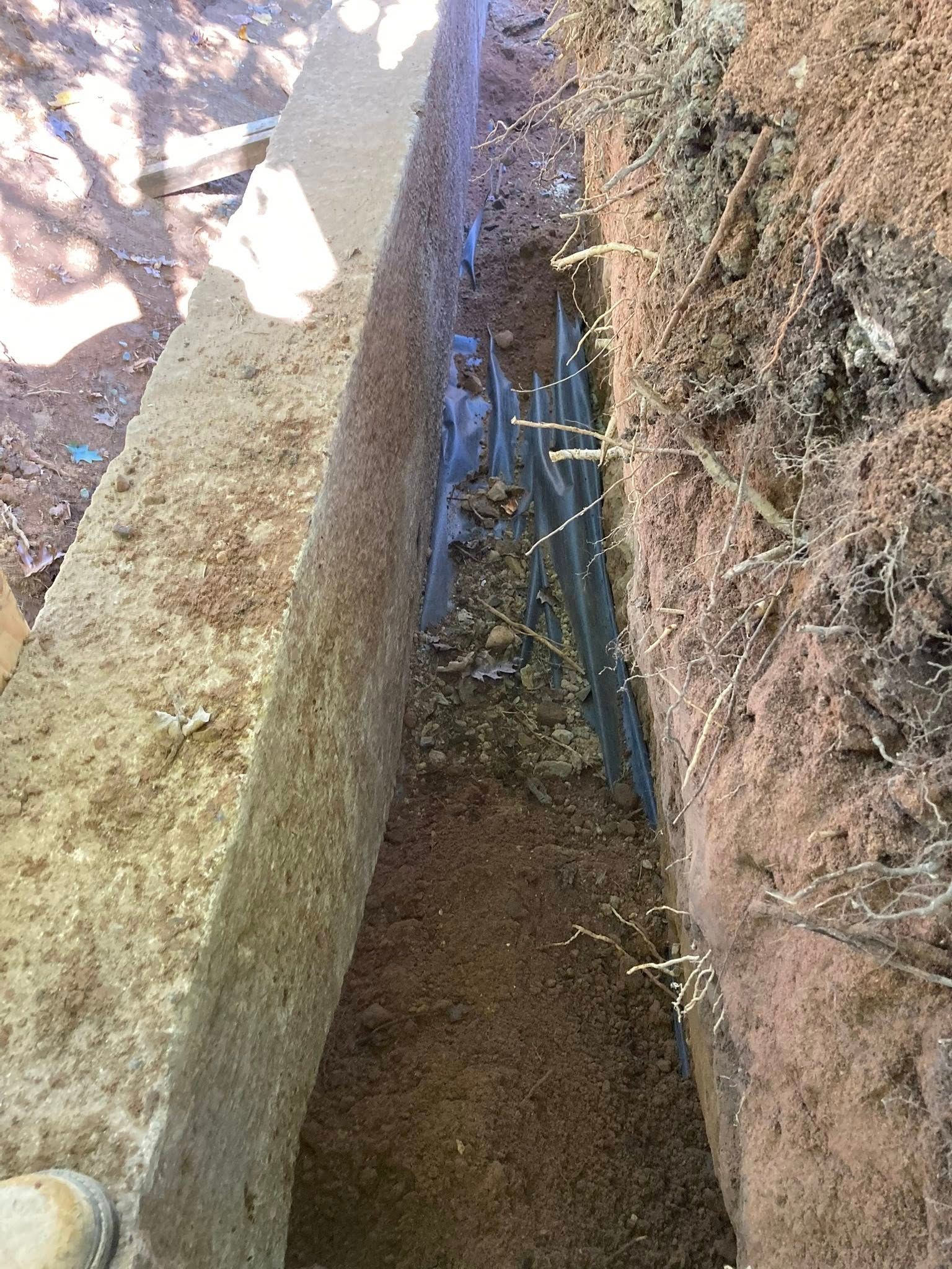 Trench with concrete edge and corrugated metal, filled with soil and roots.